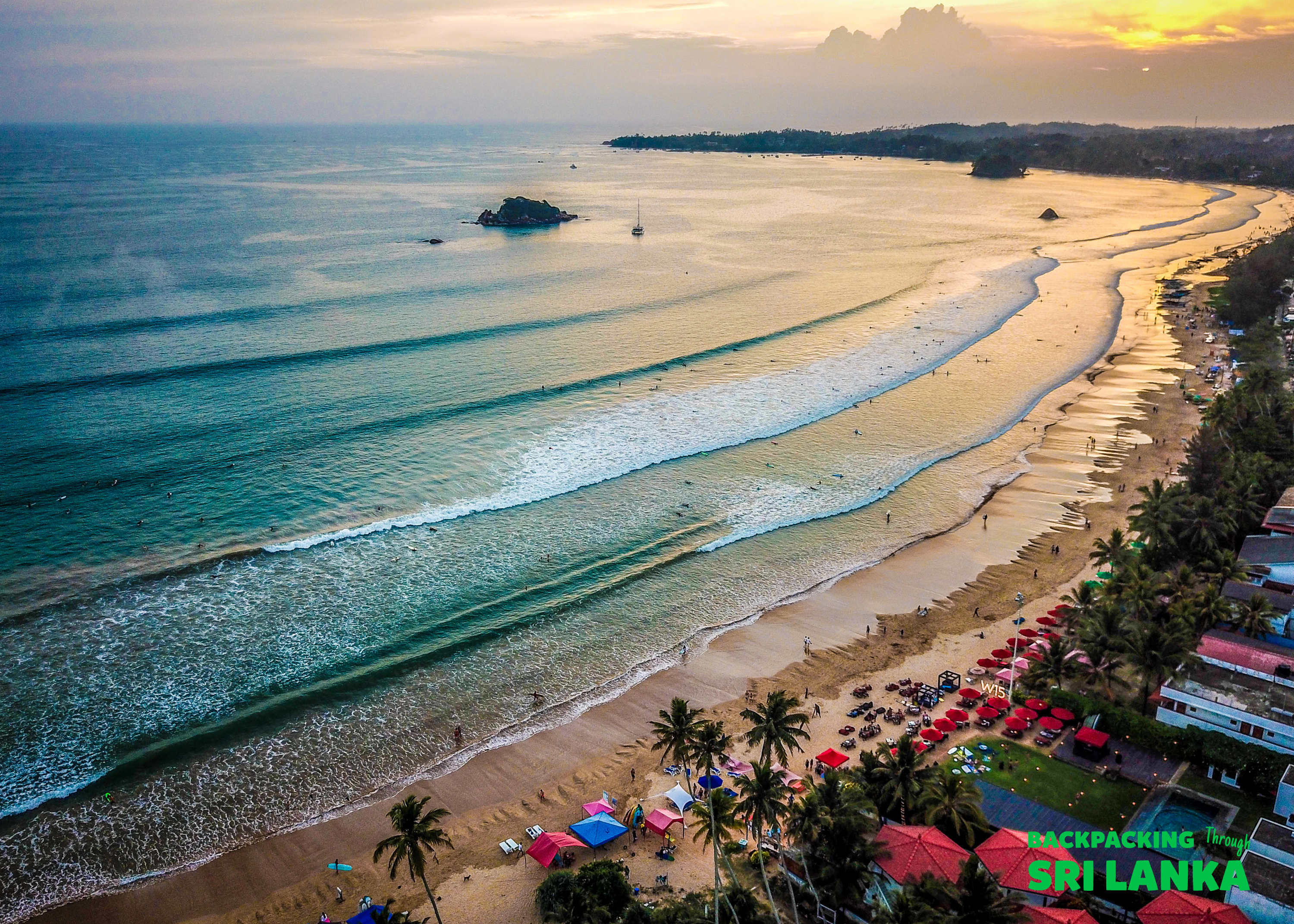 Golden hour over Weligama Beach, Sri Lanka, with many people enjoying the gentle surf.