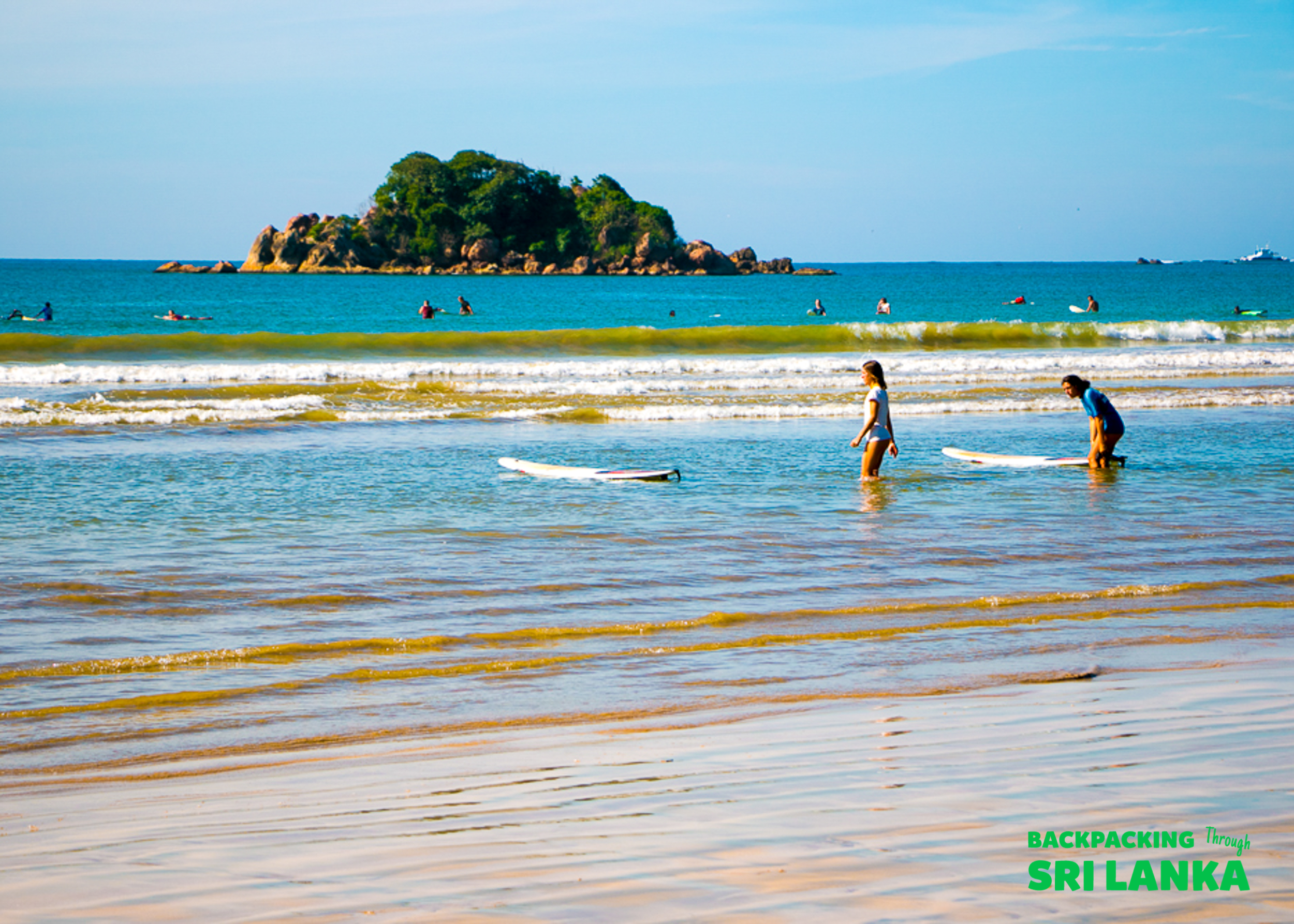 Two people with surfboards wade into the ocean for a surf lesson at Weligama, Sri Lanka.