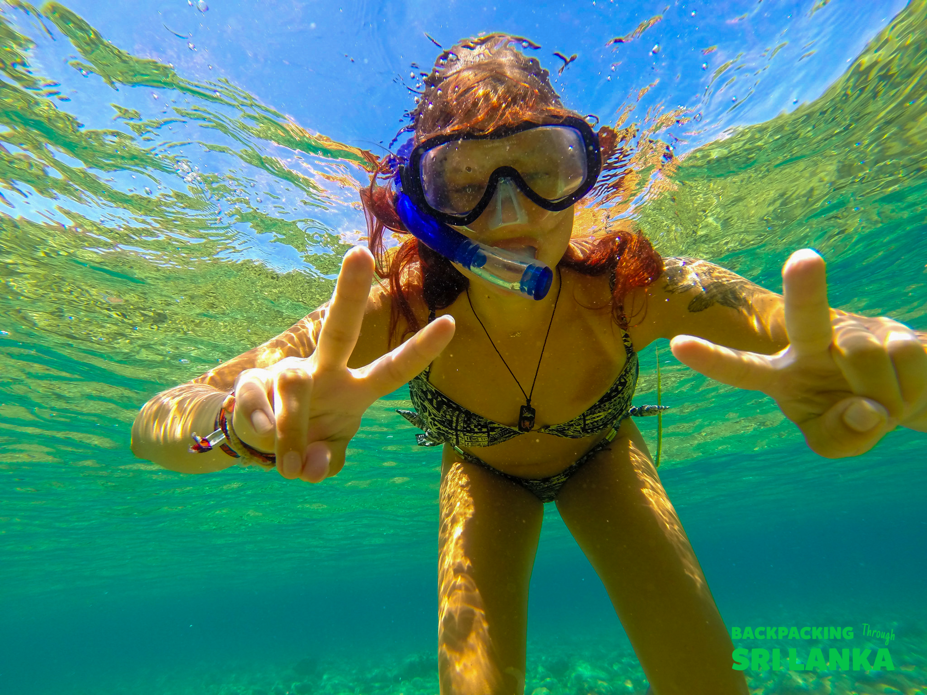 A happy woman snorkeling in clear turquoise water, making peace signs in Unawatuna, Sri Lanka.