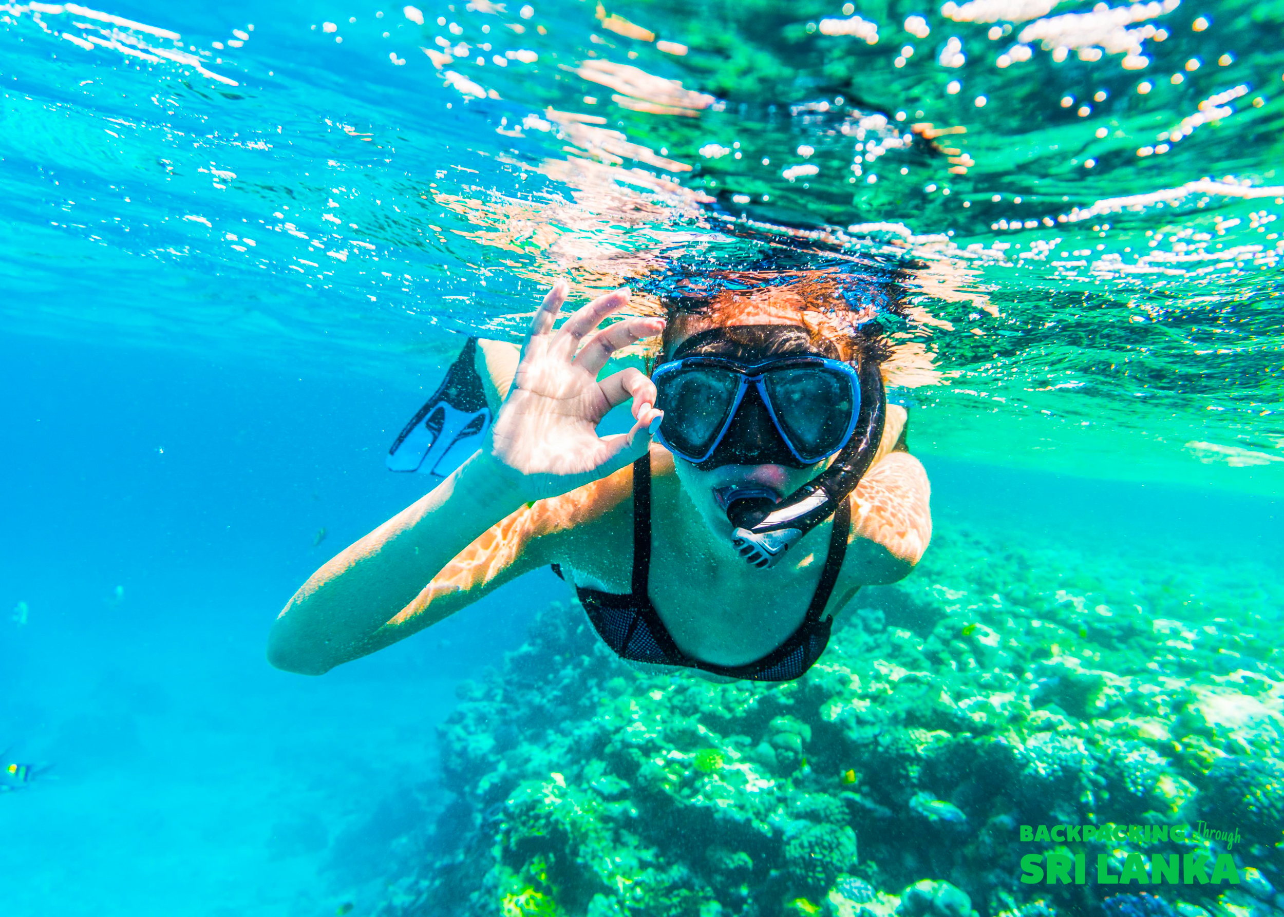 A happy snorkeler gives an OK sign underwater, exploring the vibrant coral reefs near Unawatuna.