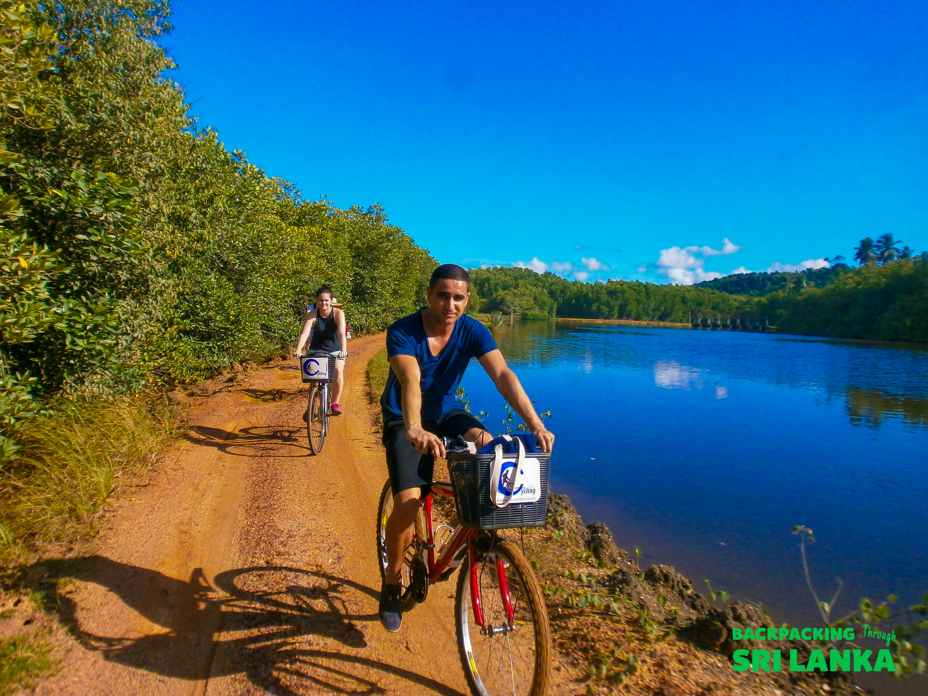 Enjoying a cycle tour along a scenic dirt path next to a beautiful blue lake in Sri Lanka.