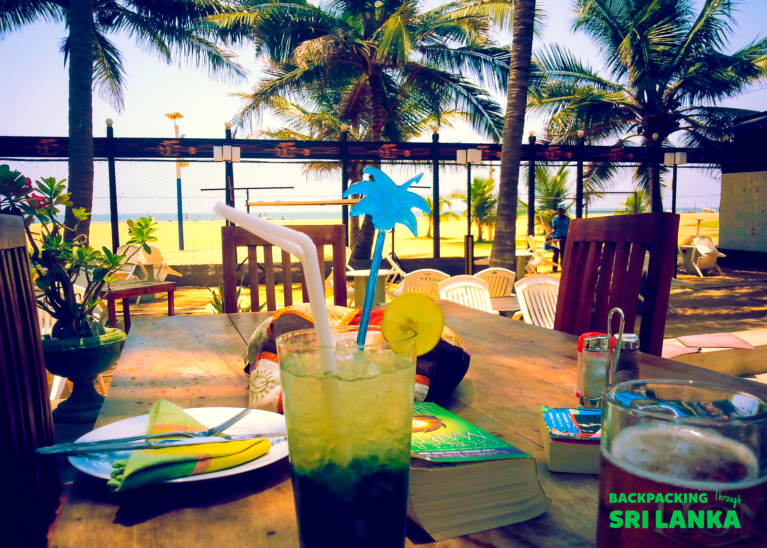 Enjoying a refreshing drink at a beachside cafe in Unawatuna, Sri Lanka, with palm trees and ocean views.