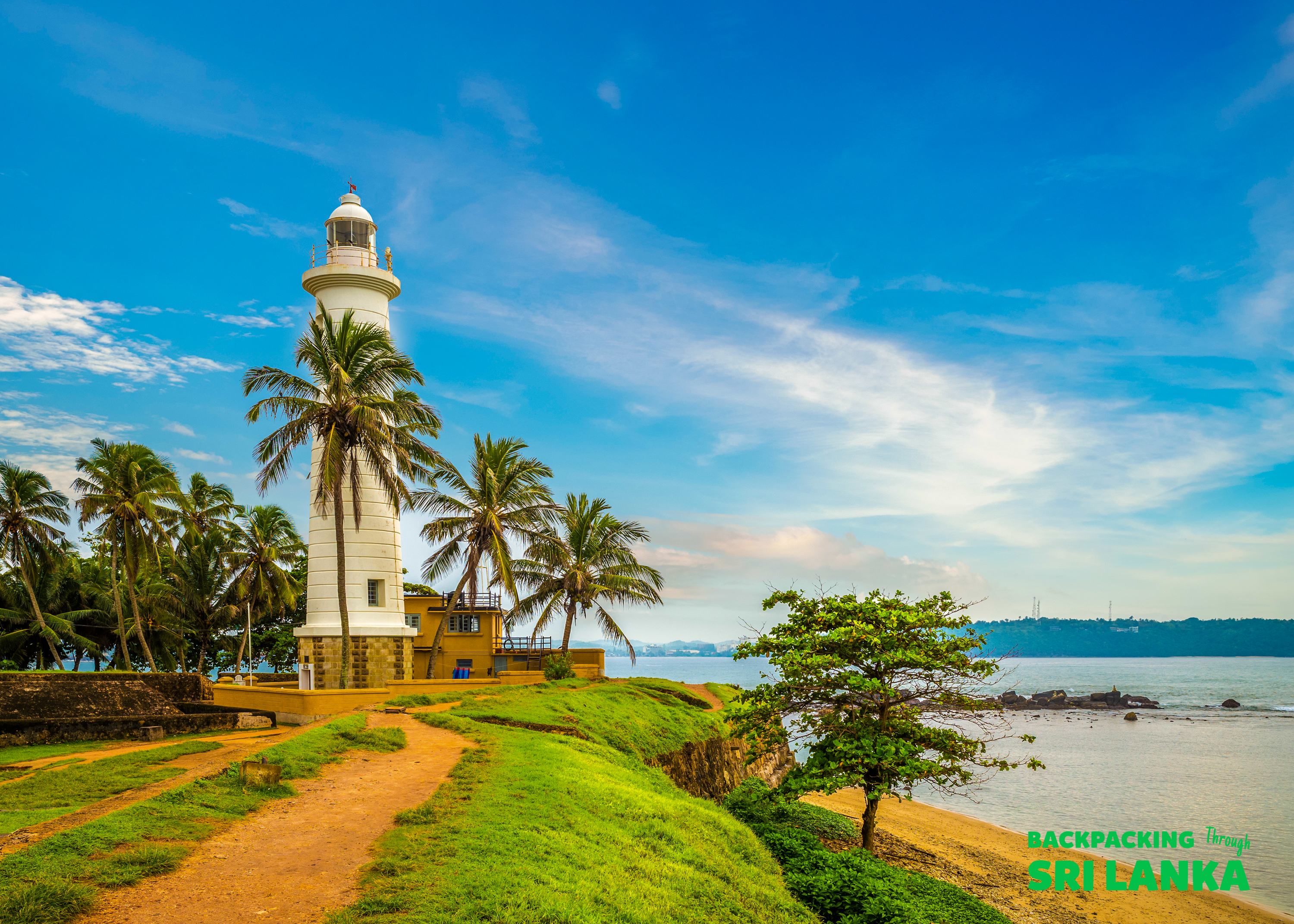 The magnificent white lighthouse at Galle Fort stands tall, surrounded by palm trees and the ocean.