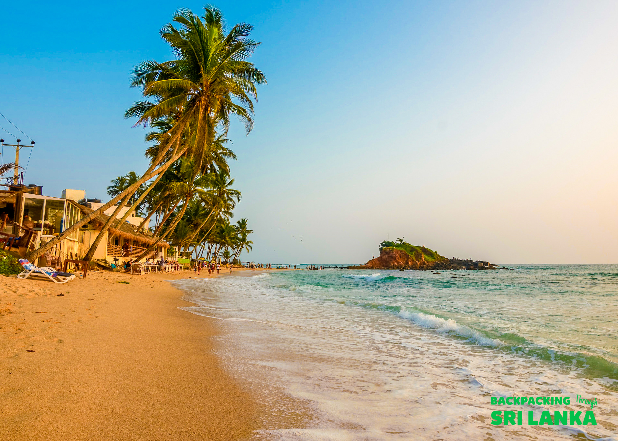 Golden sand beach with leaning palm trees, gentle waves, and a small island near Galle, Sri Lanka.