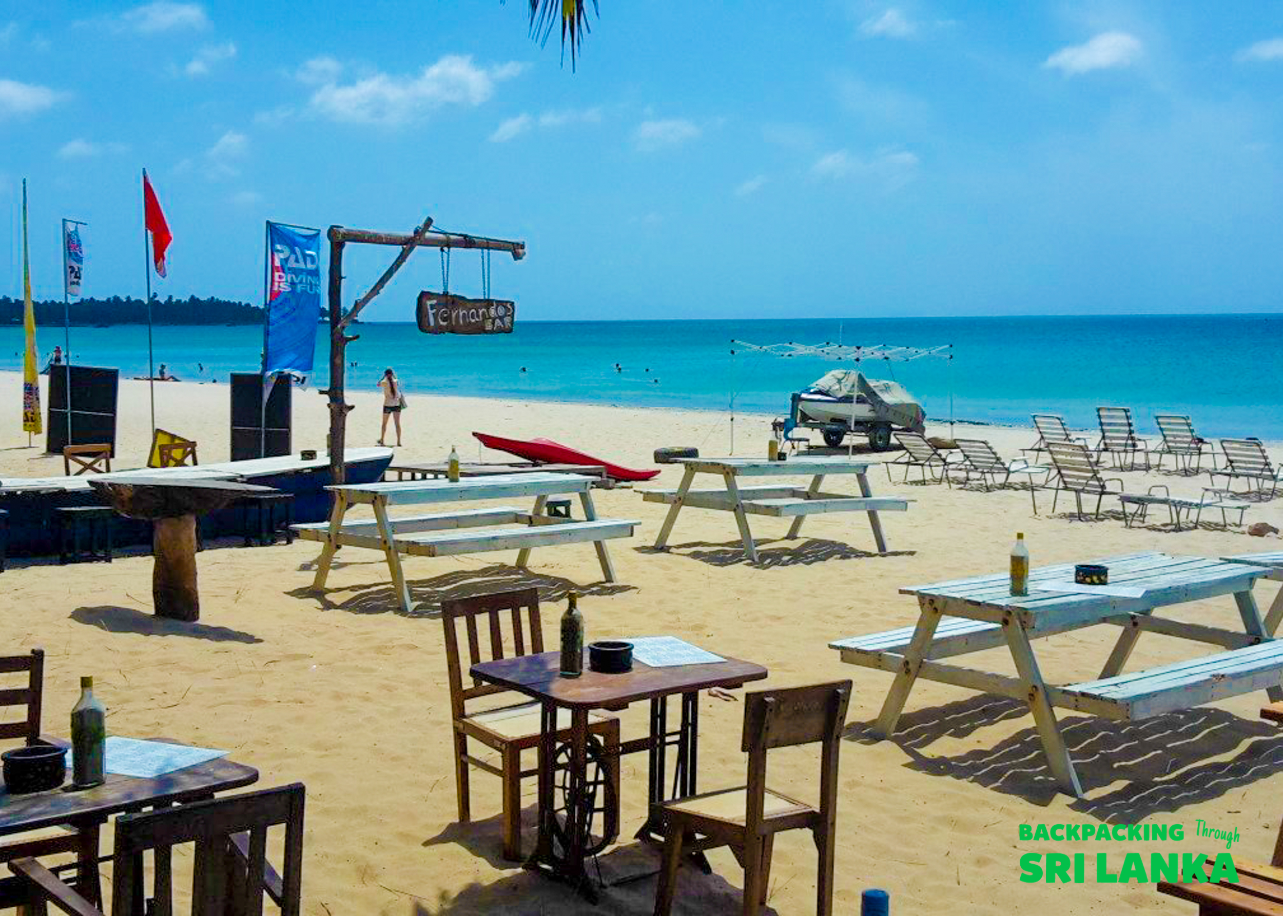 Relaxing tropical beach with wooden tables and picnic benches on the sand, facing the turquoise sea.