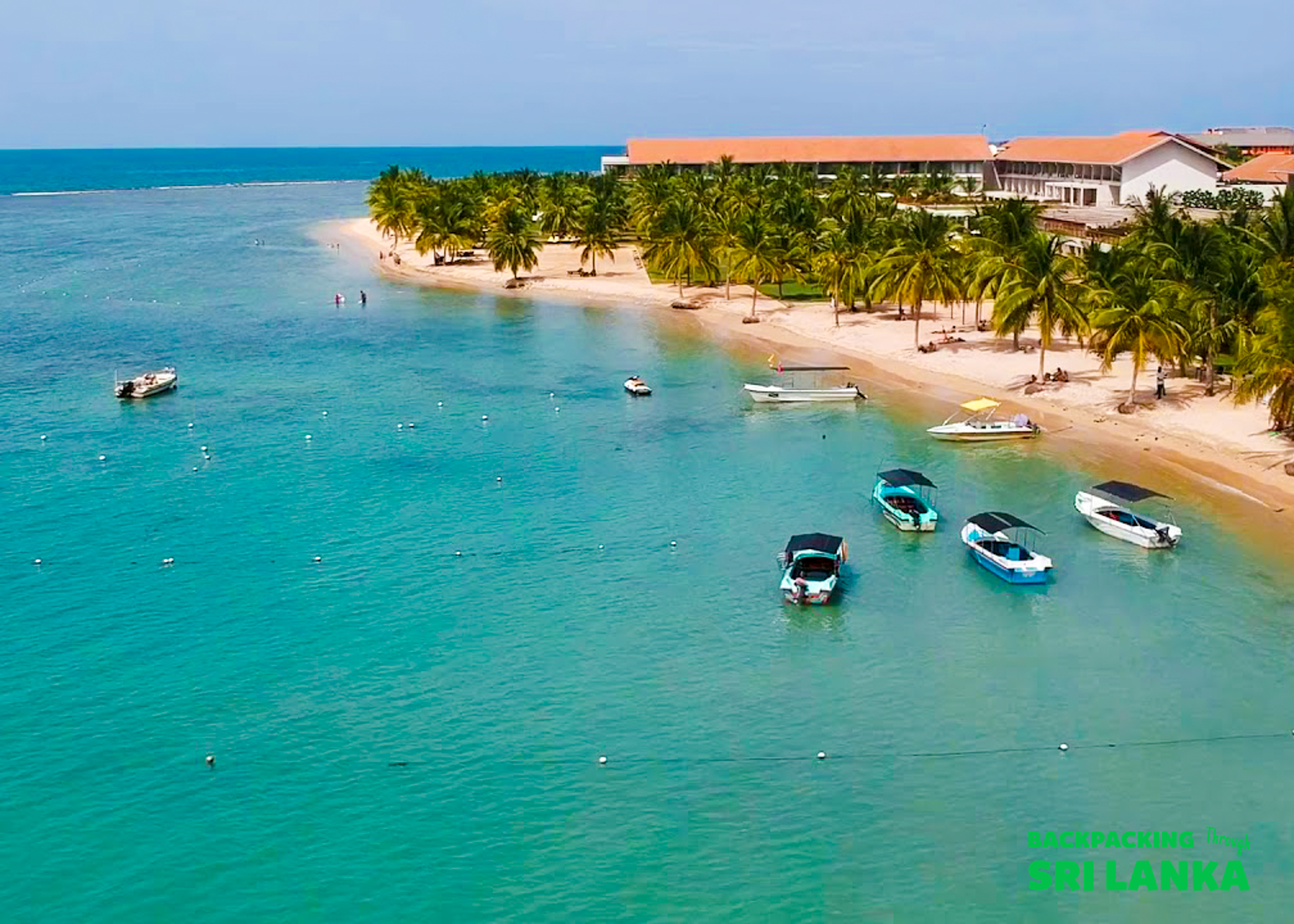 Tropical beach in Sri Lanka with boats on turquoise water, palm trees, and a resort.