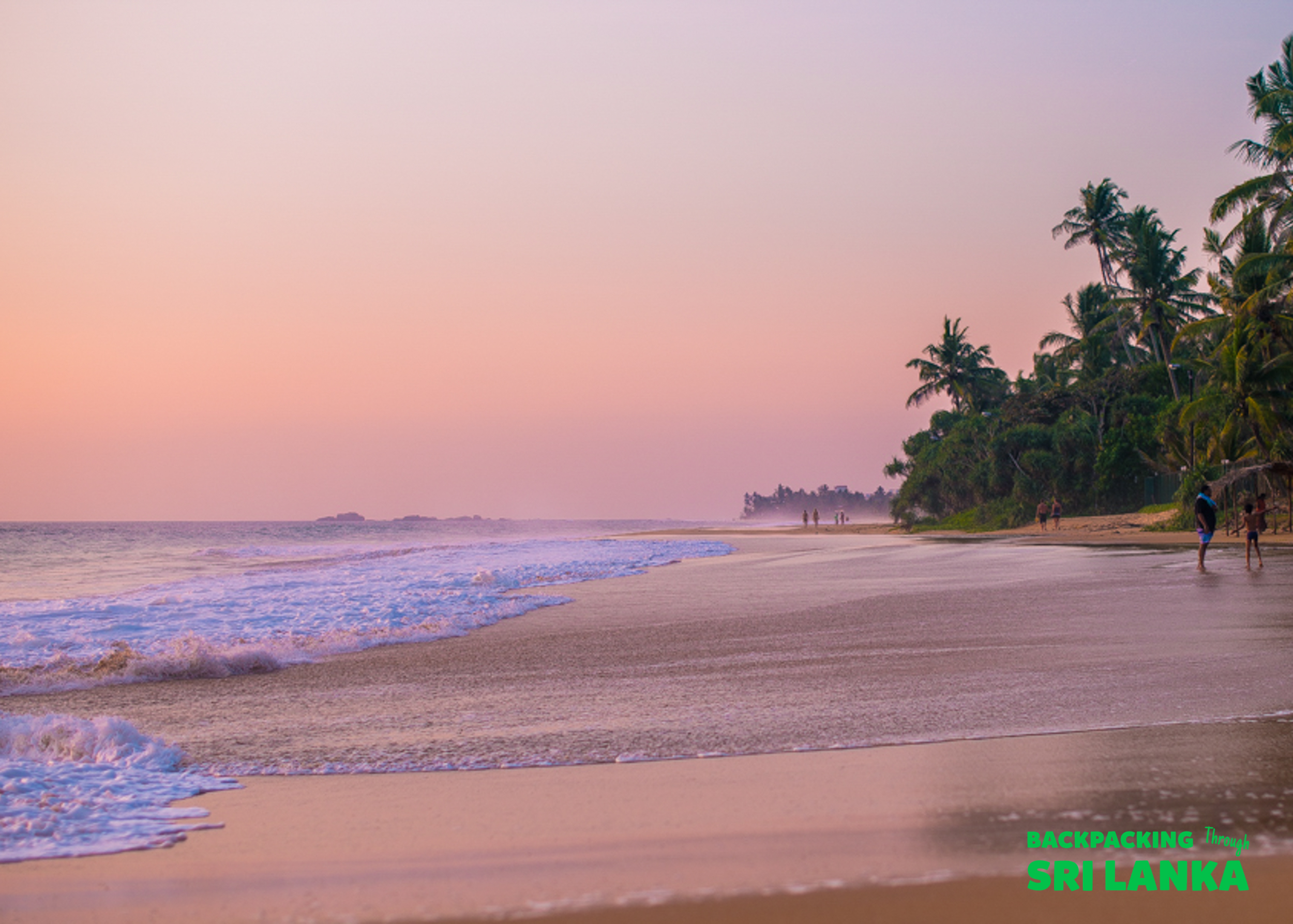 Sunset over a tranquil sandy beach with gentle waves and palm trees near Galle, Sri Lanka.