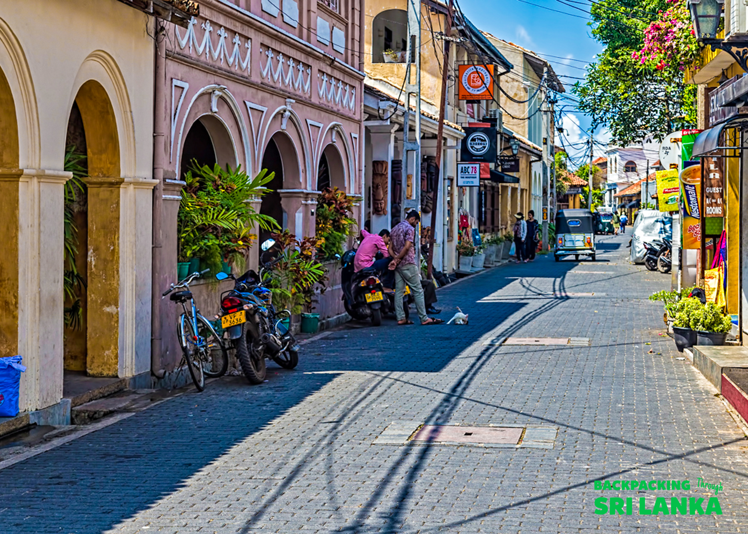 People gather on a narrow street in Galle, Sri Lanka, lined with historic colonial buildings.
