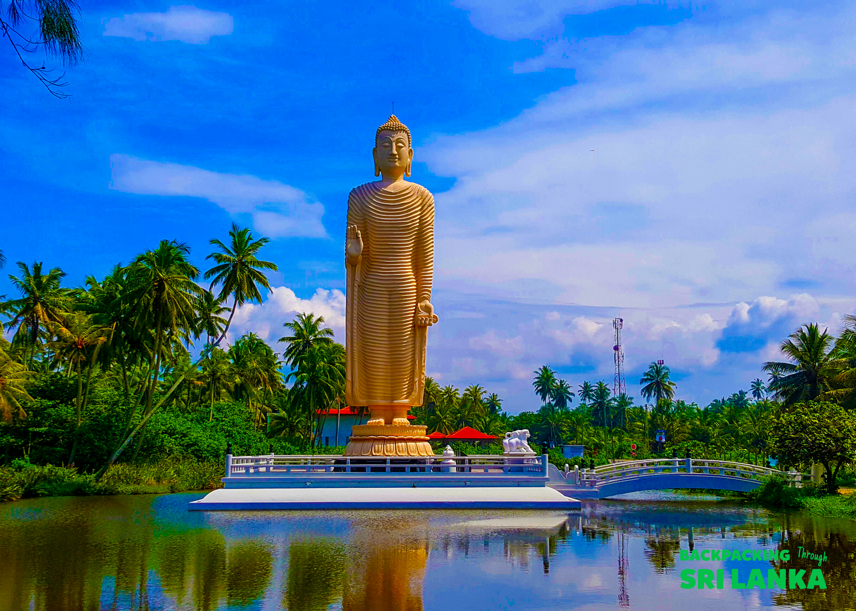 A majestic golden Buddha statue stands tall, reflected in calm water at the Peraliya Tsunami Memorial.