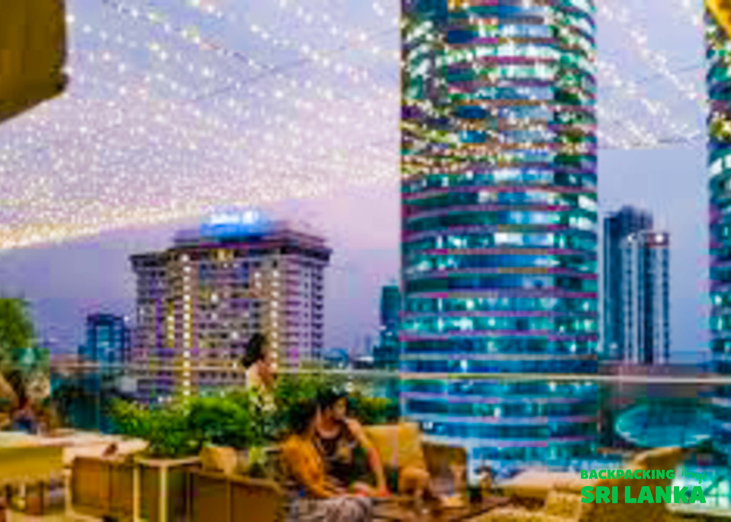 Two people relax on a rooftop bar, enjoying the illuminated city skyline of Colombo.