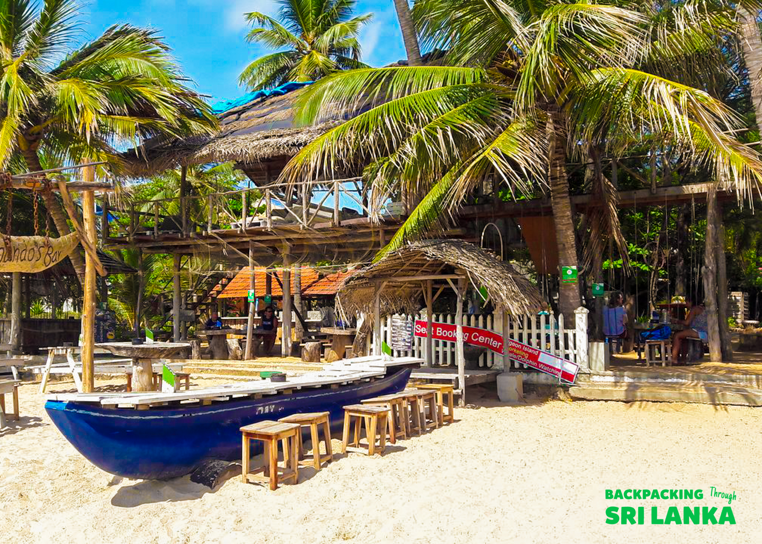 Relaxing beach scene with a blue boat, stools, palm trees, and thatched buildings in Colombo.