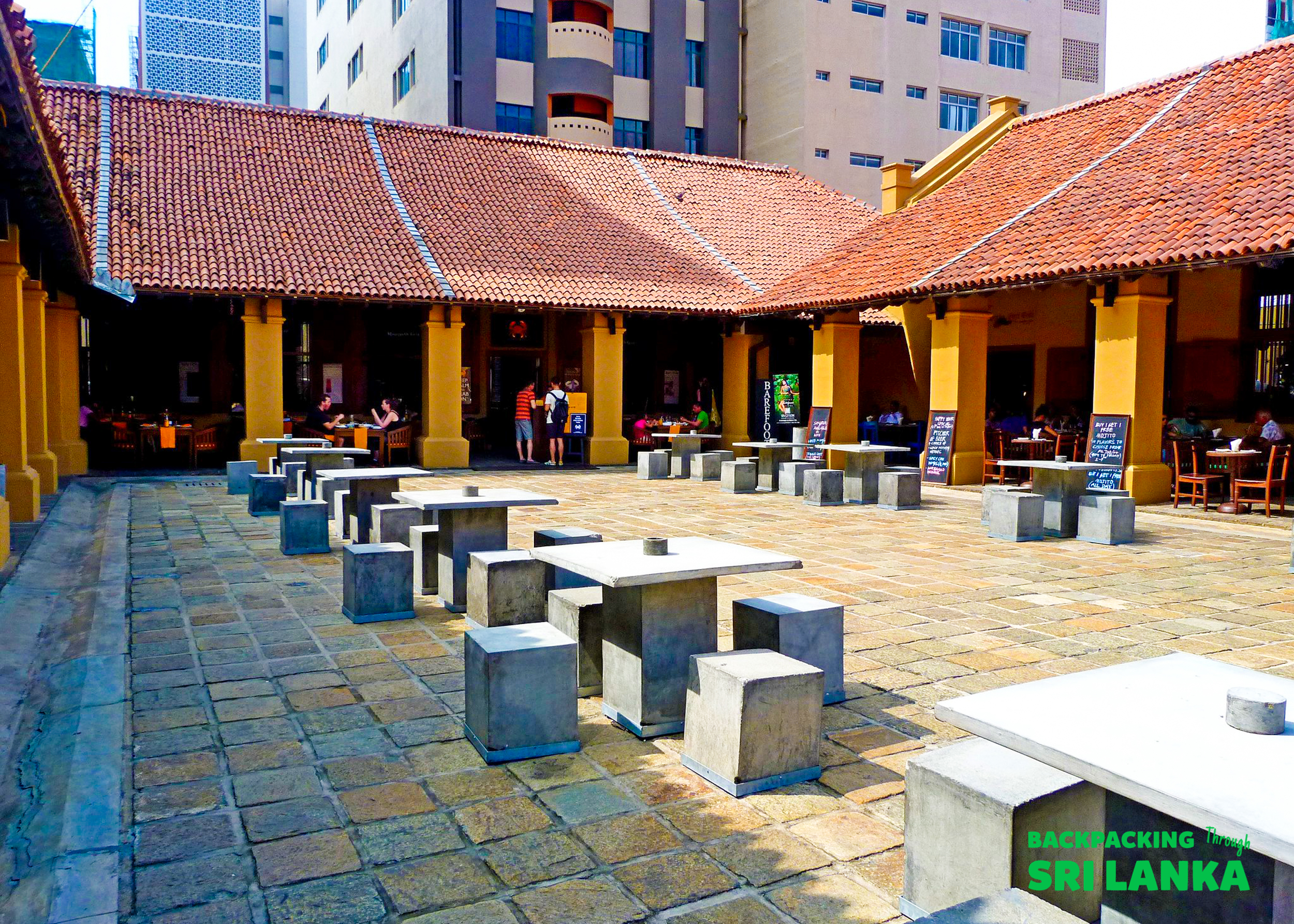 People relax at an open-air courtyard cafe with stone tables and traditional architecture in Colombo.