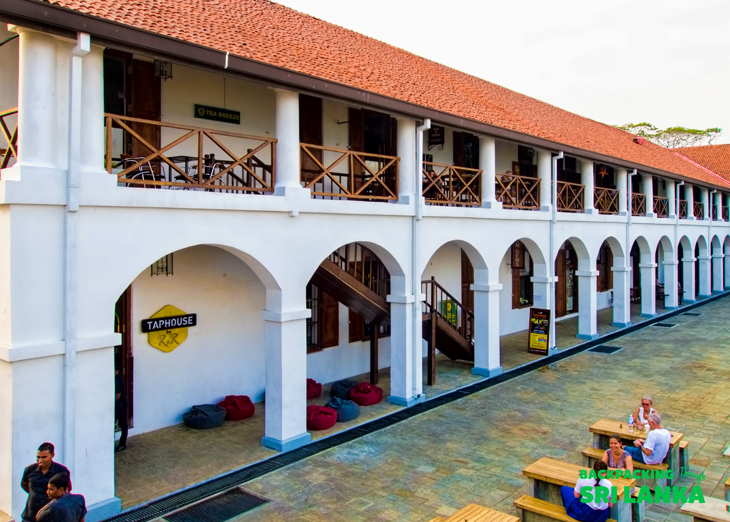 People relaxing and socializing at an outdoor taphouse with historic arched colonial architecture in Colombo.