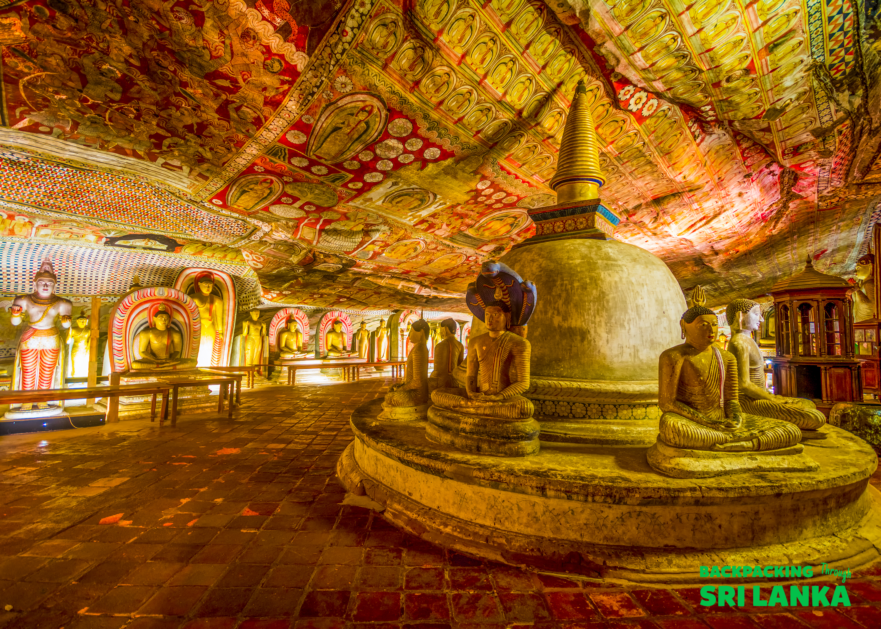 Inside the Dambulla Cave Temple, ancient Buddha statues line the walls under a vibrantly painted ceiling.