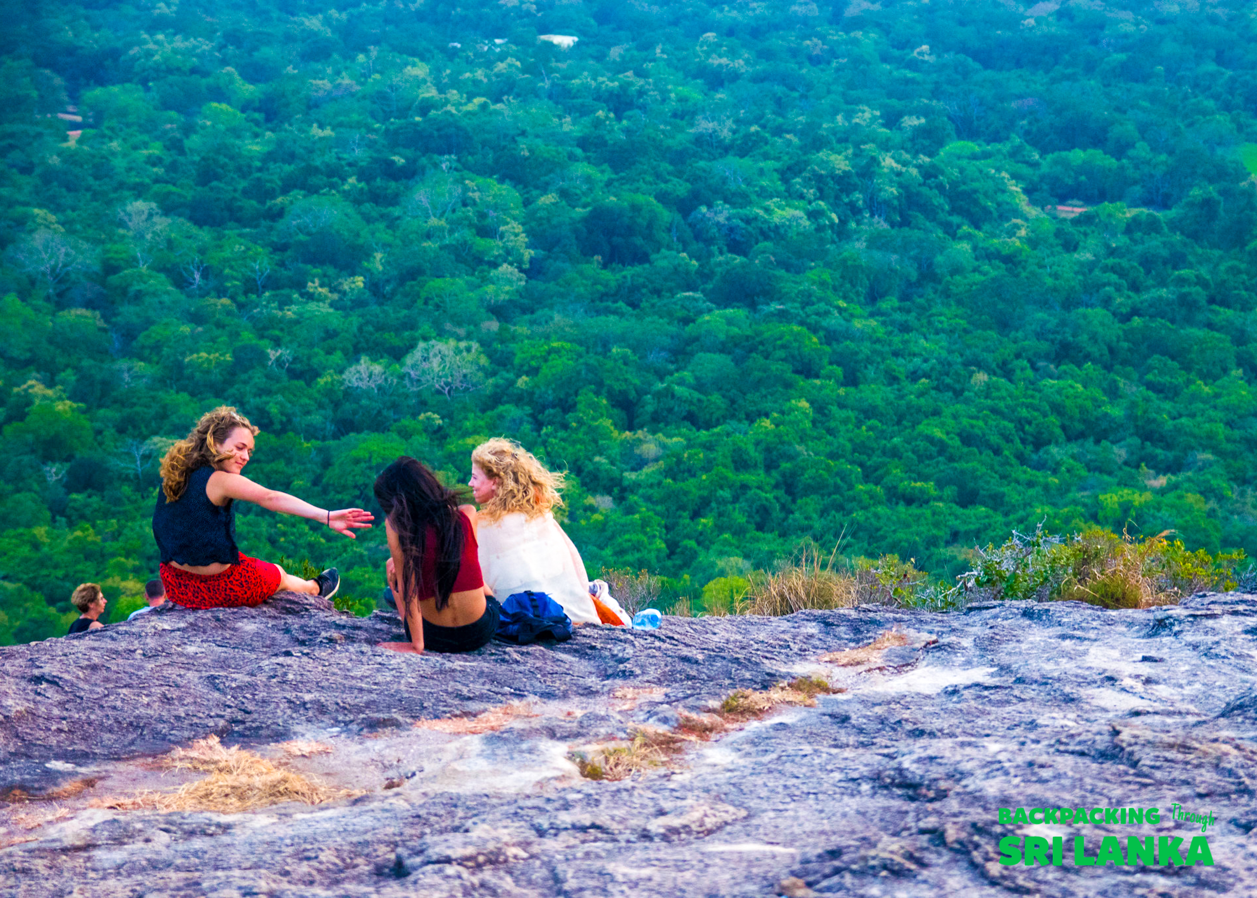 Friends share a moment on a scenic rock overlooking the lush green jungle near Dambulla.
