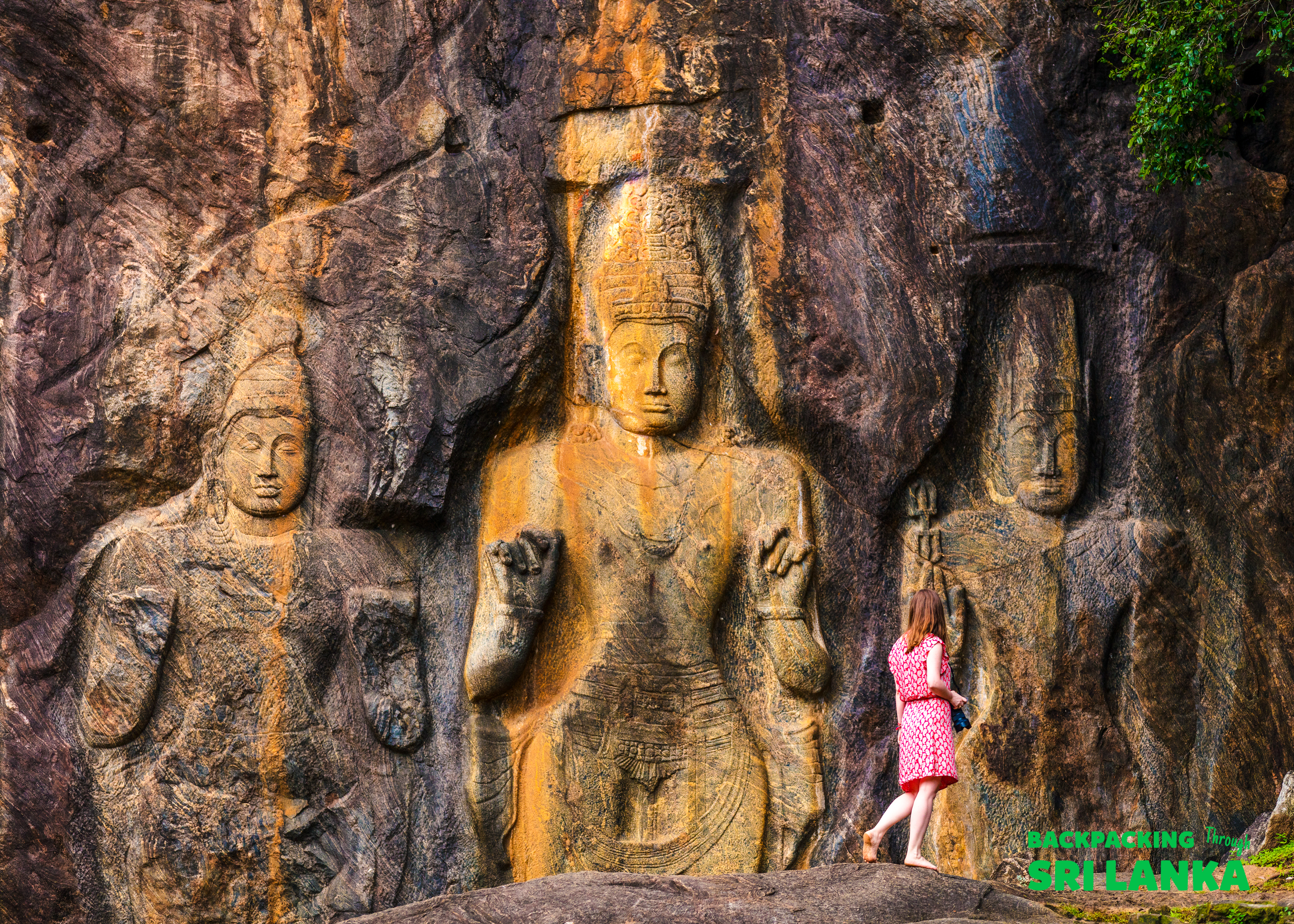 A woman in a pink dress stands next to monumental ancient rock carvings at Sigiriya, Sri Lanka.