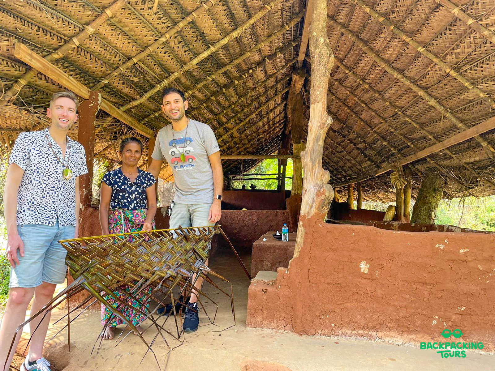 Two men and a local woman with a woven craft under a rustic thatched roof in Sigiriya.
