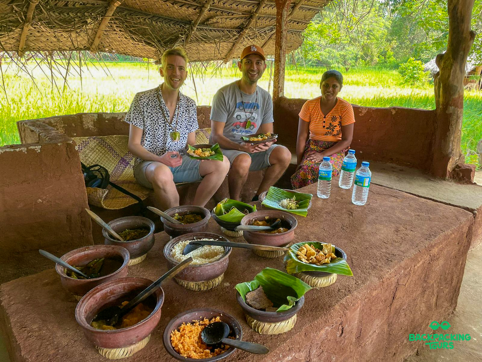 Travelers and a local host share an authentic Sri Lankan village meal under a thatched roof in Sigiriya.