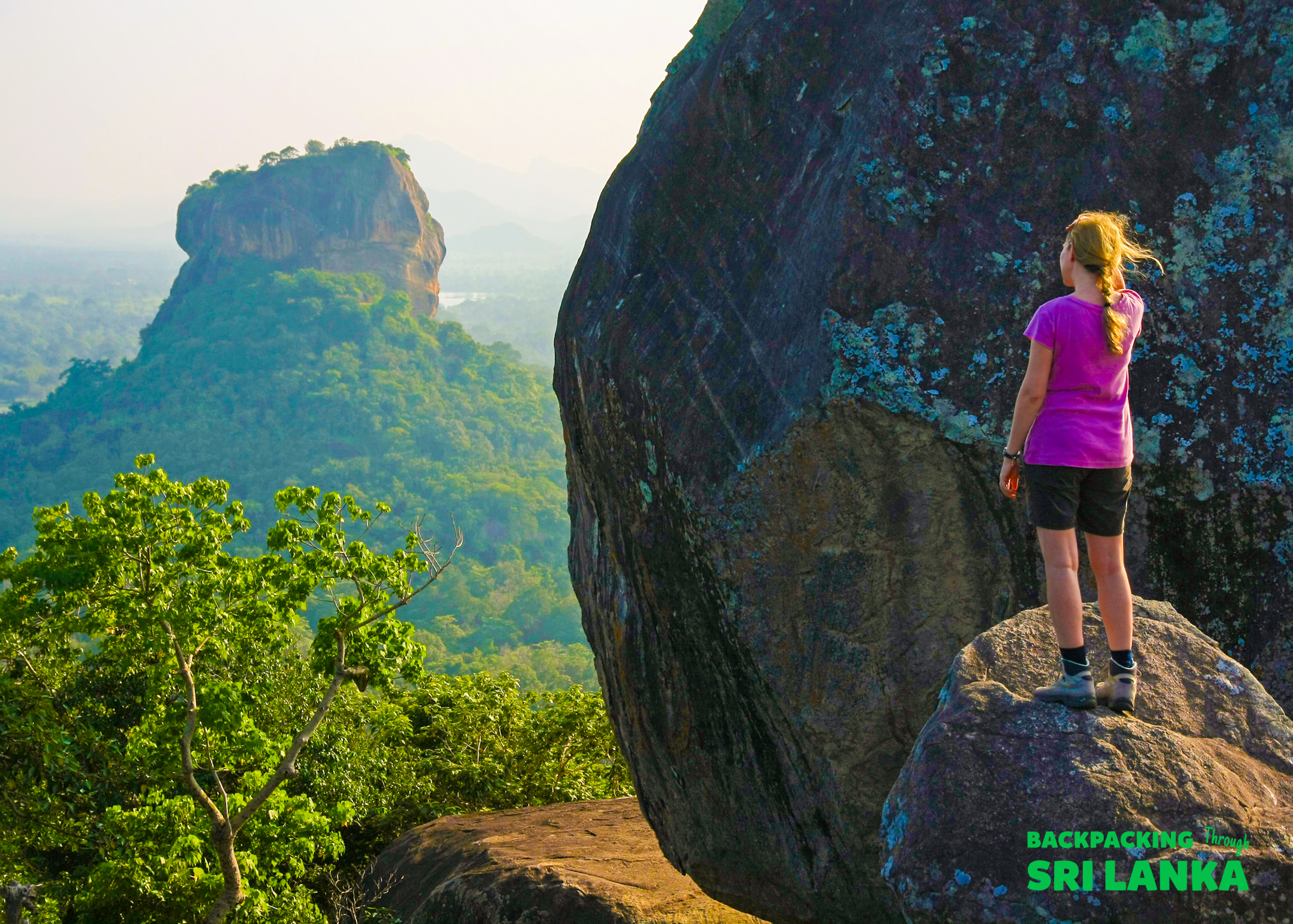 A backpacker stands on a rock, admiring the iconic Sigiriya Rock and lush landscape of Sri Lanka.