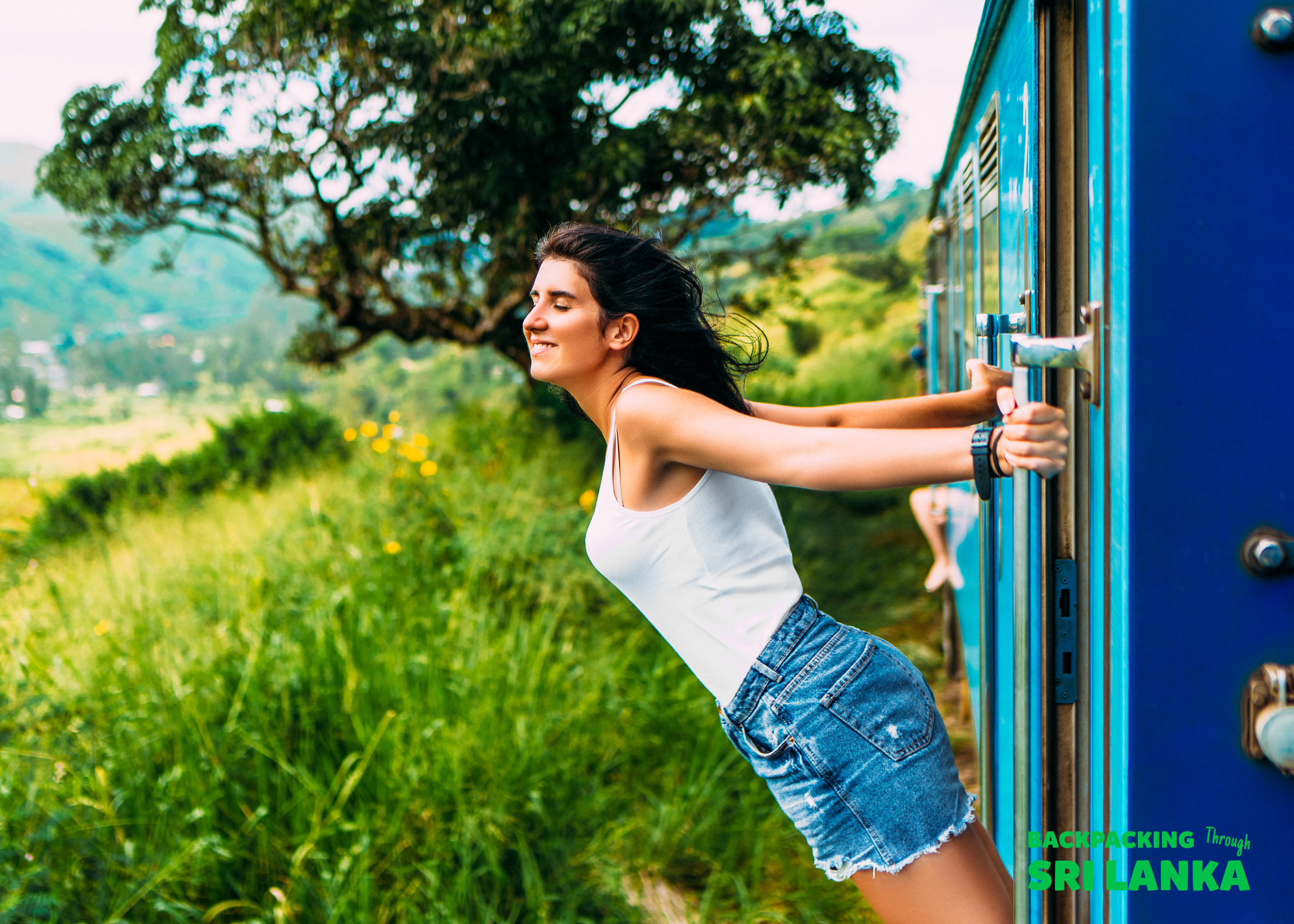 A joyful woman leans from a blue train, enjoying the scenic tea plantations of Sri Lanka.