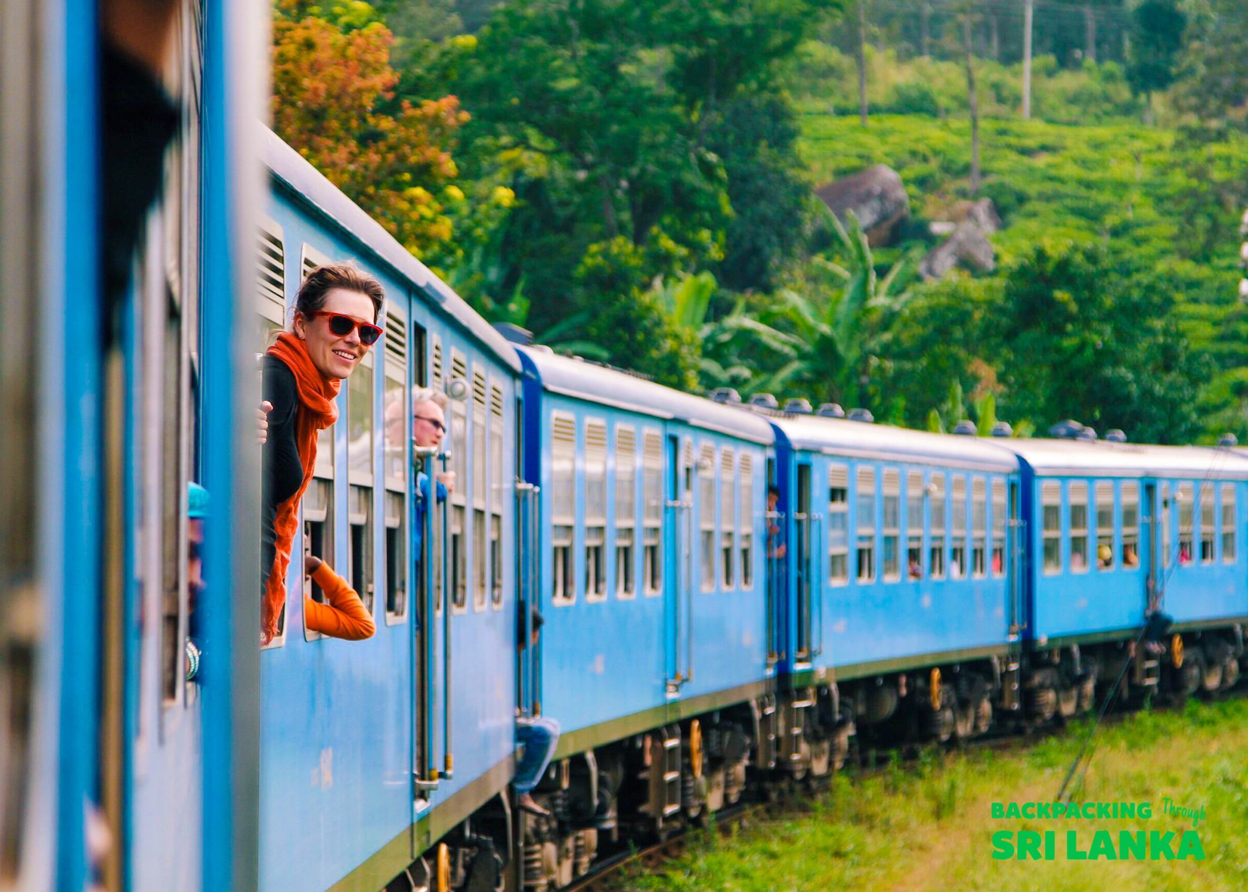 Happy travelers lean out of a blue train window, enjoying the scenic ride through Sri Lanka's tea plantations.