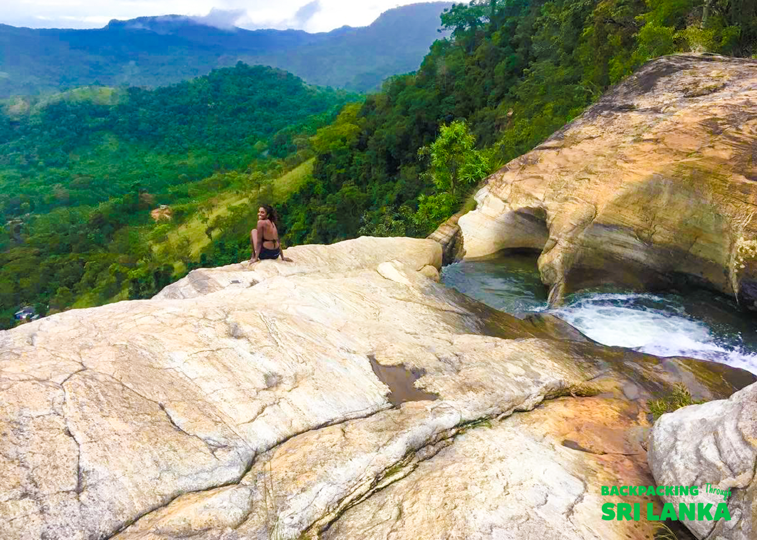 A person sits on a rock ledge at Diyaluma Falls, overlooking the lush green valley in Sri Lanka.
