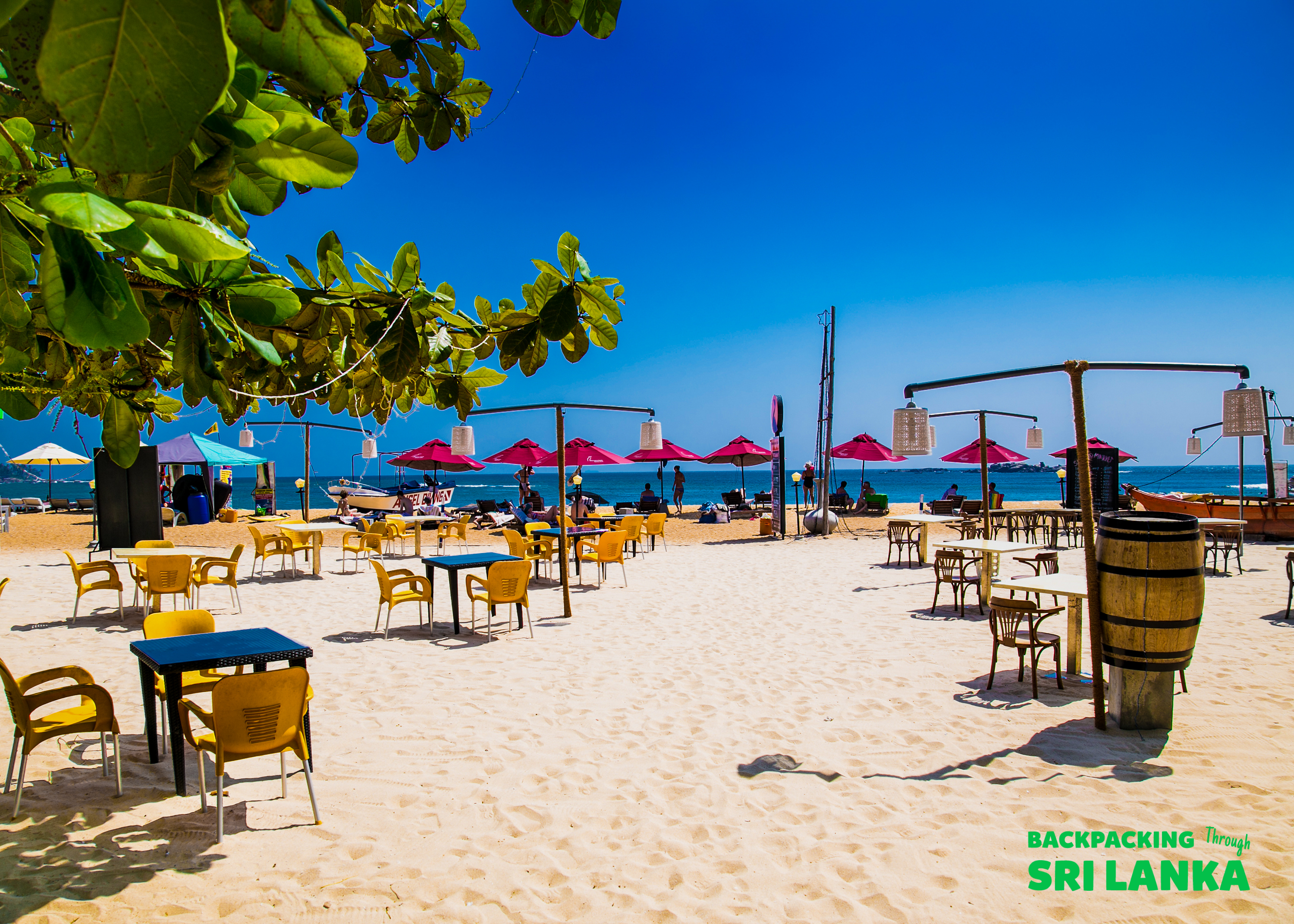 Bright sunny day on Weligama beach with many empty tables and chairs set up for dining.