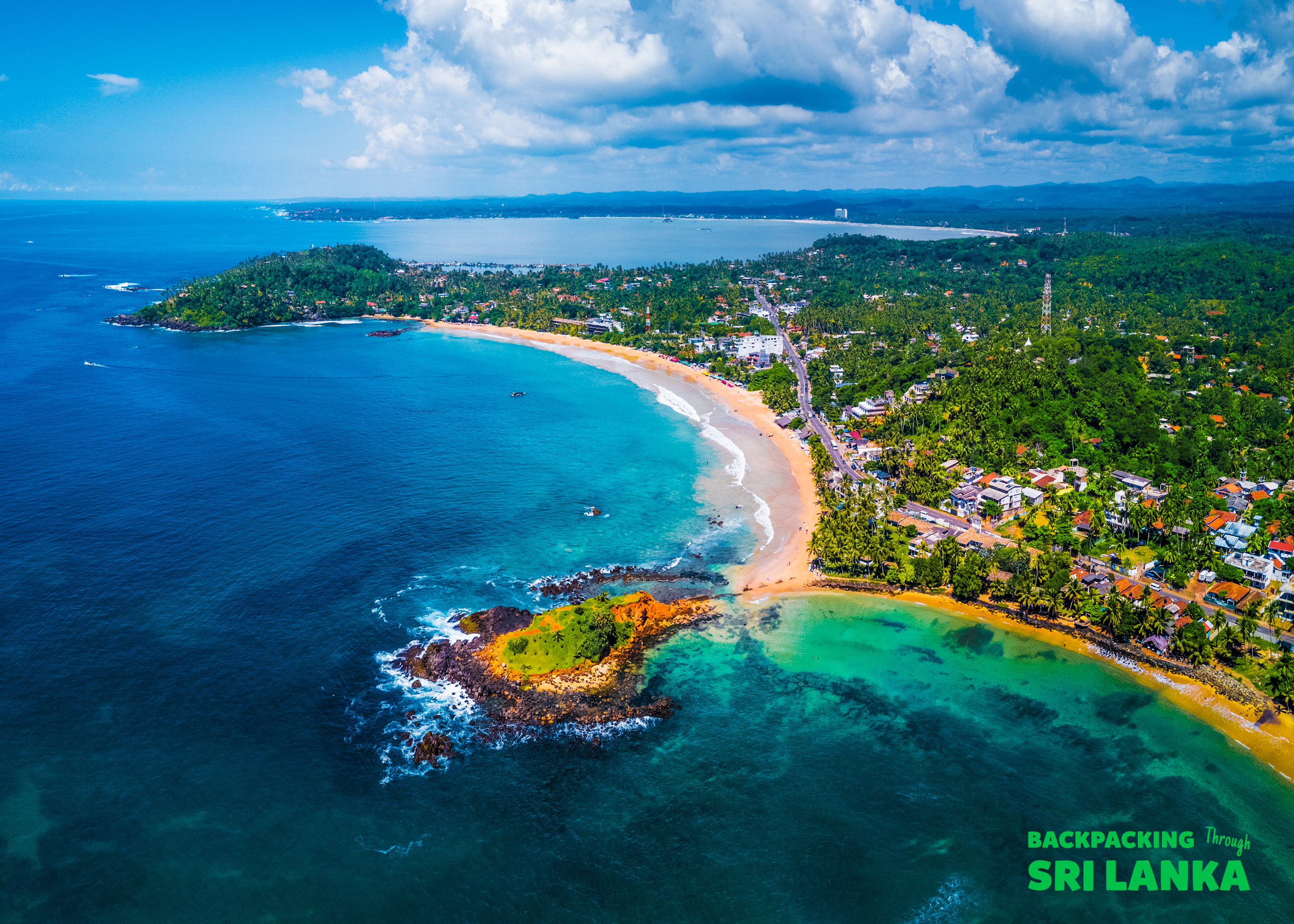 Weligama's picturesque coastline with a long sandy beach, clear turquoise water, and lush greenery.