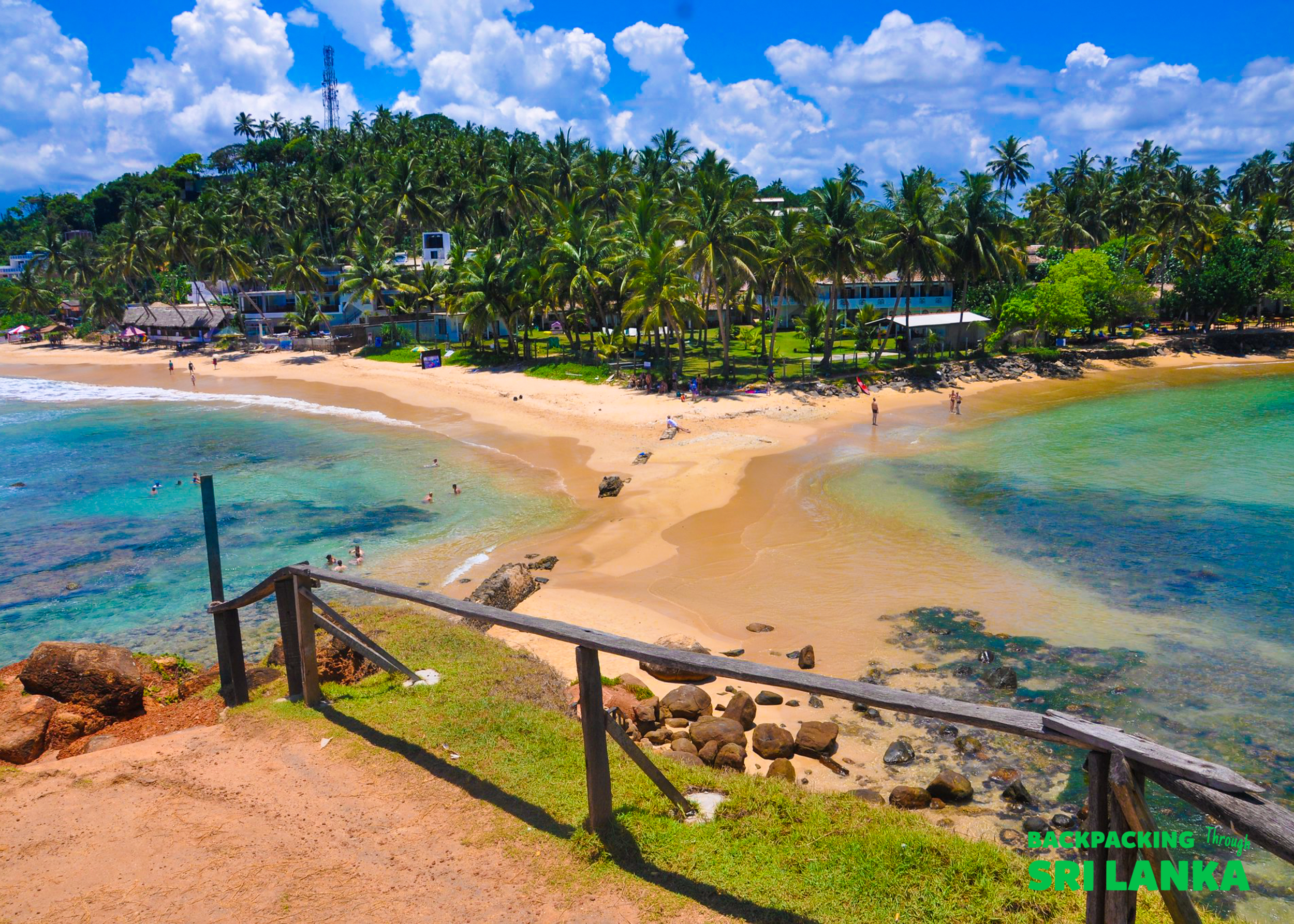 A scenic view of Weligama beach in Sri Lanka, with clear turquoise water and lush palm trees.