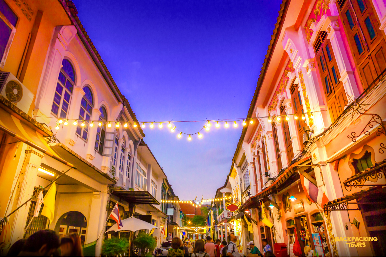 A charming street in Phuket Old Town at twilight, with string lights illuminating colorful Sino-Portuguese buildings.