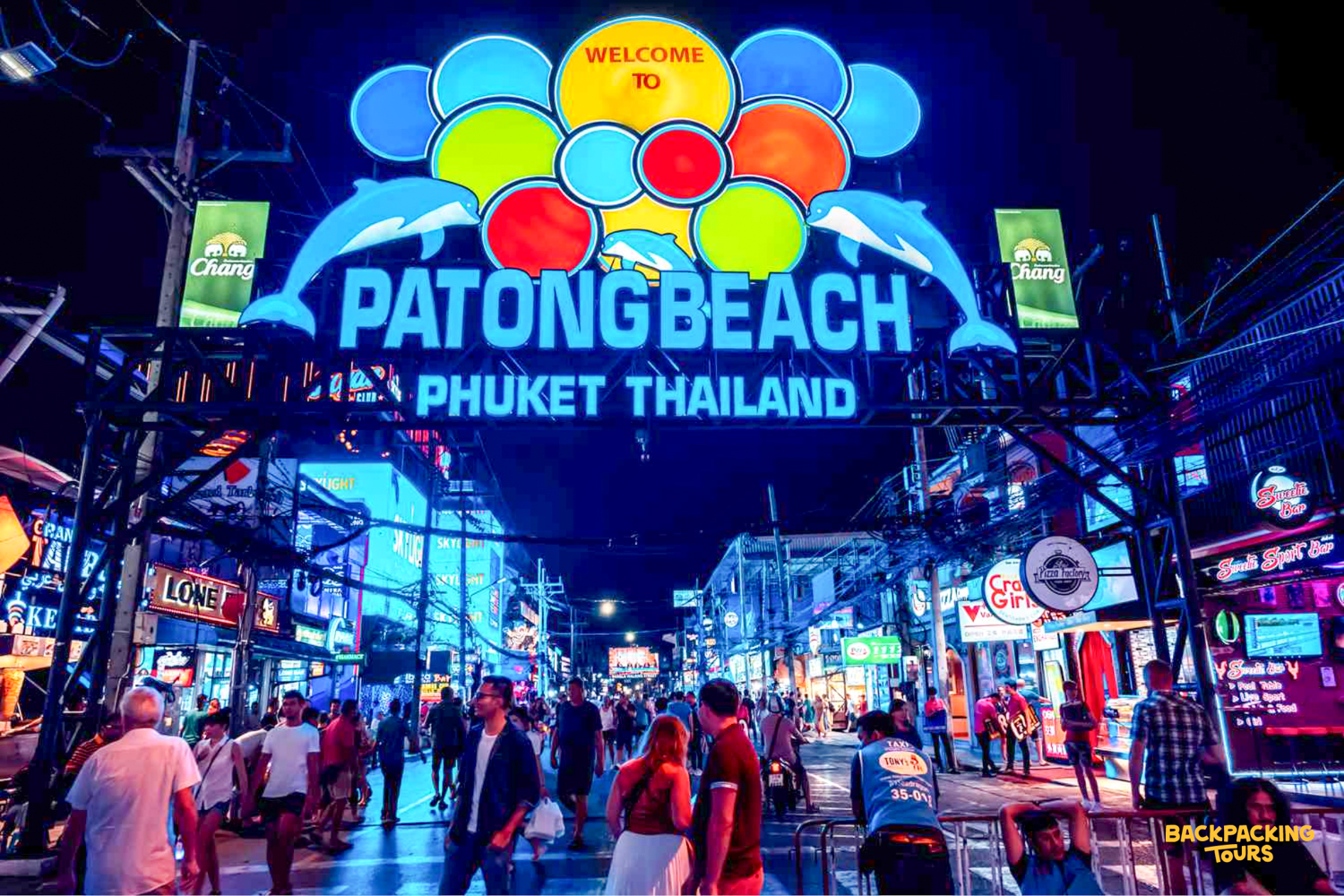 Vibrant Patong Beach, Phuket, Thailand, at night, with a brightly lit welcome sign and lively crowds.