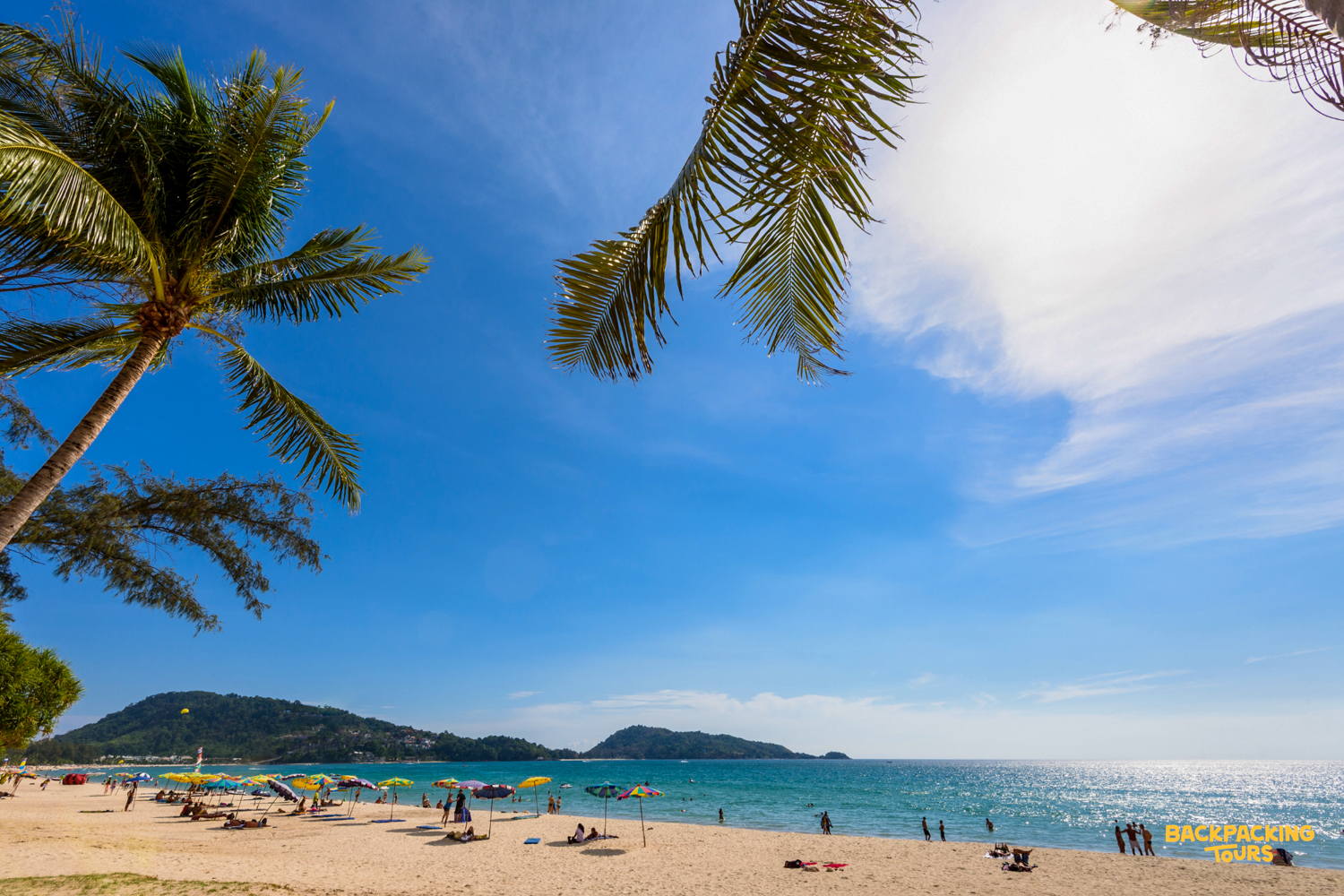 Relaxing on the sandy Patong Beach in Phuket with palm trees and a bright blue sky.