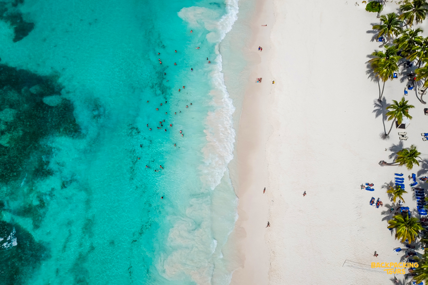 Aerial view of a vibrant turquoise ocean meeting a white sandy beach with palm trees in Phuket.