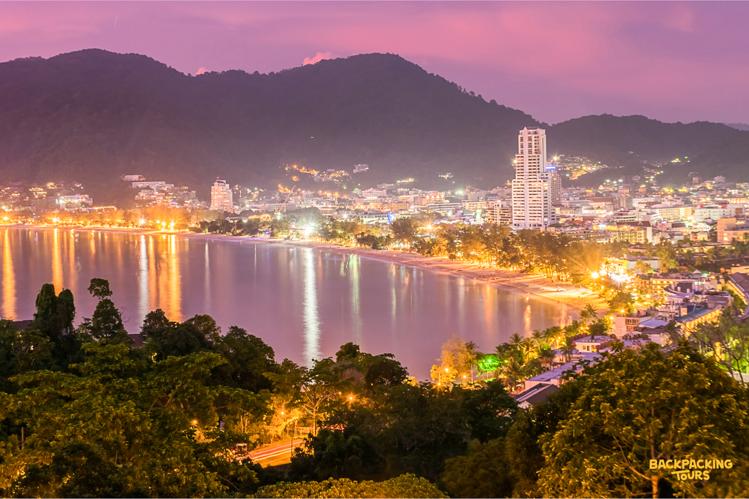 Vibrant Patong Beach in Phuket, Thailand, illuminated at dusk with city lights reflecting on the calm bay.