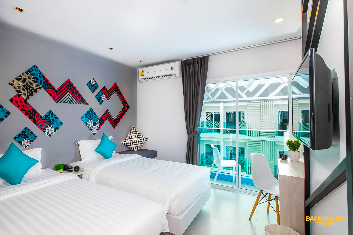A clean, contemporary twin room in Phuket, featuring vibrant wall art and a private balcony.