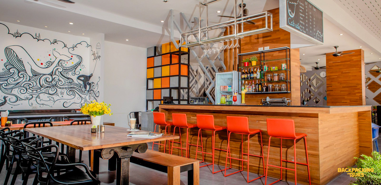 A vibrant hostel common room in Phuket with a whale mural, wooden tables, and orange bar stools.