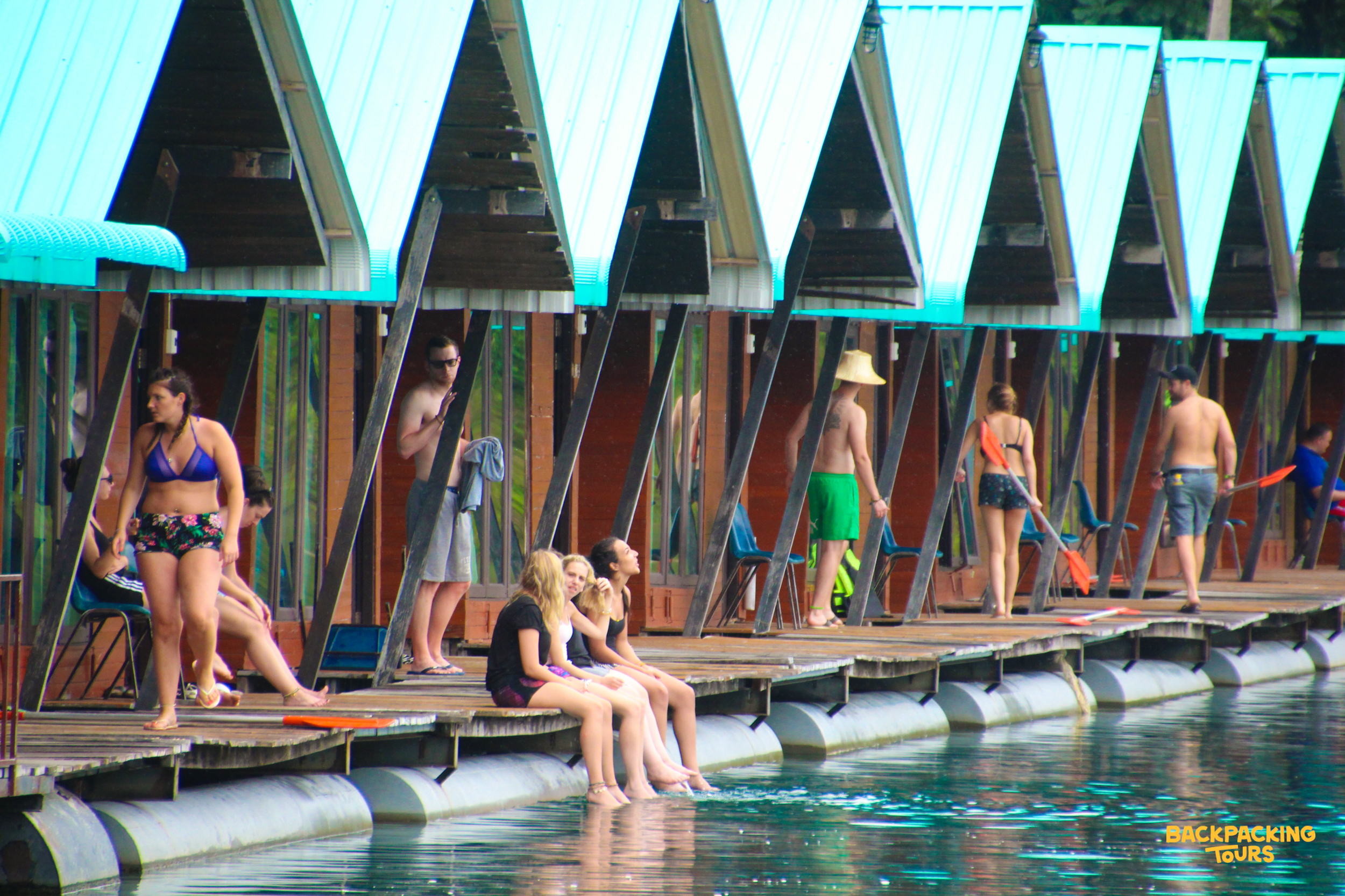 Backpacking group relaxing on raft house deck by lake.
