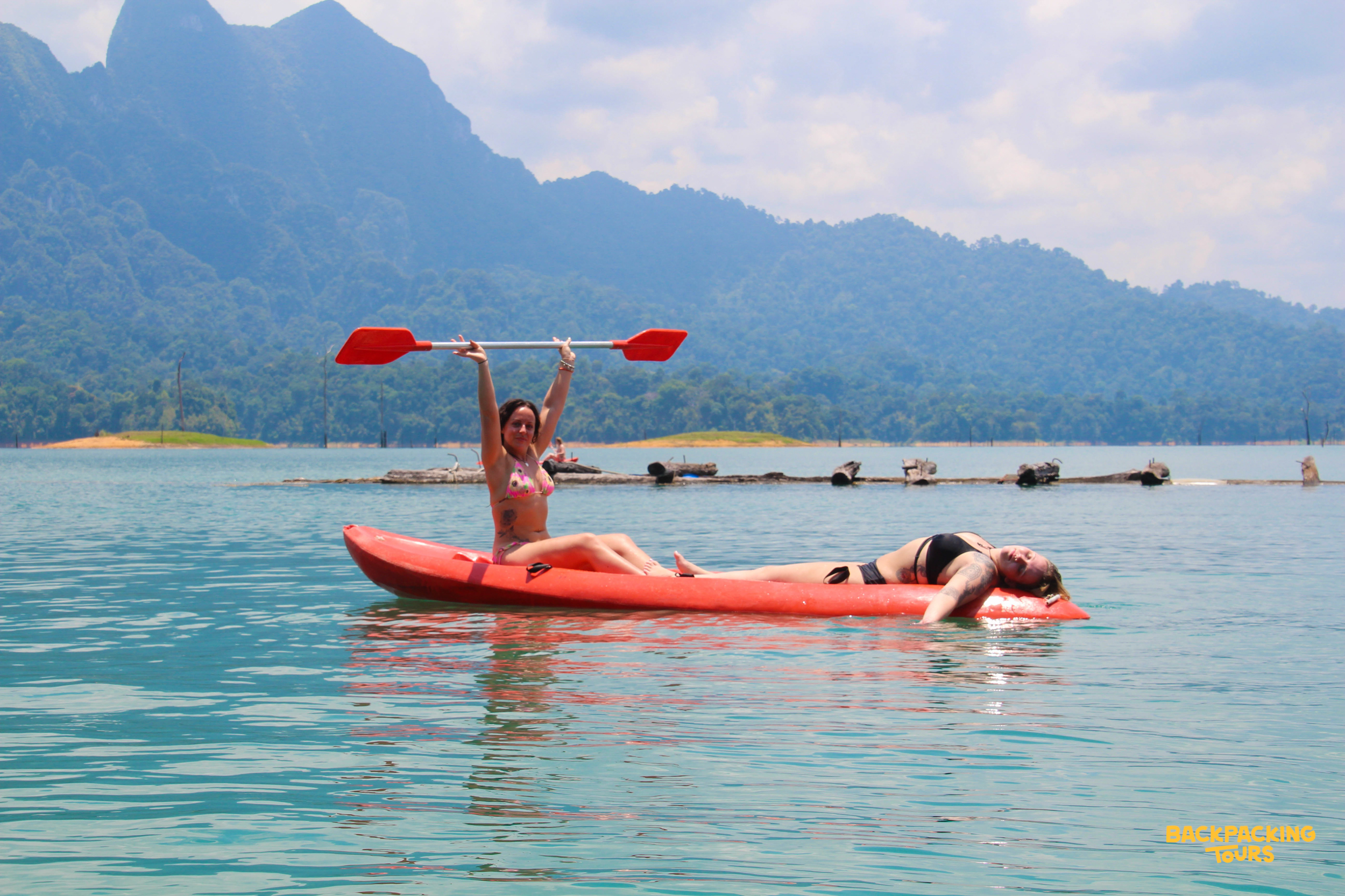 Travelers paddling red kayaks on emerald water in Thailand.