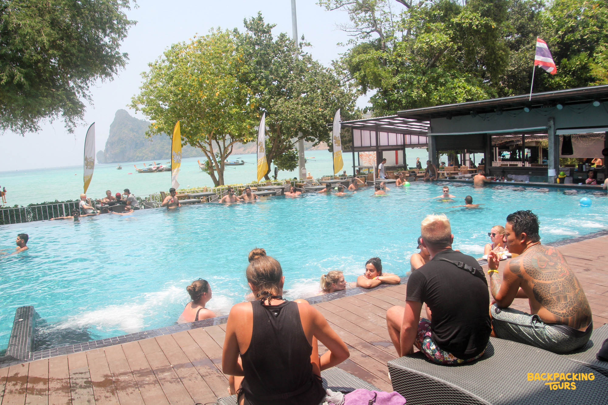 Tourists relax and swim in a vibrant pool overlooking the stunning turquoise waters of Koh Phi Phi.
