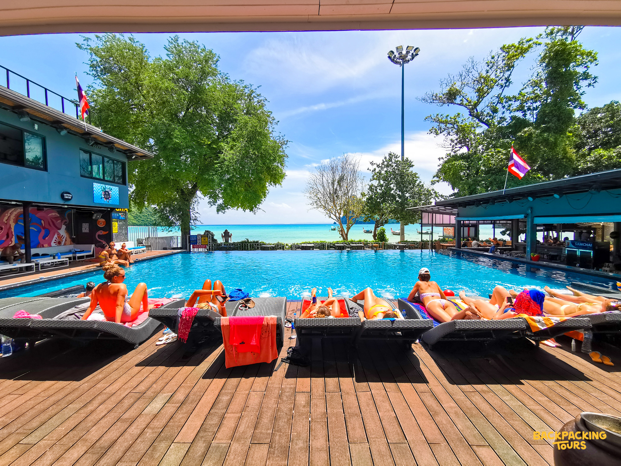 People relax on sun loungers by a resort pool overlooking the beautiful blue ocean in Koh Phi Phi.