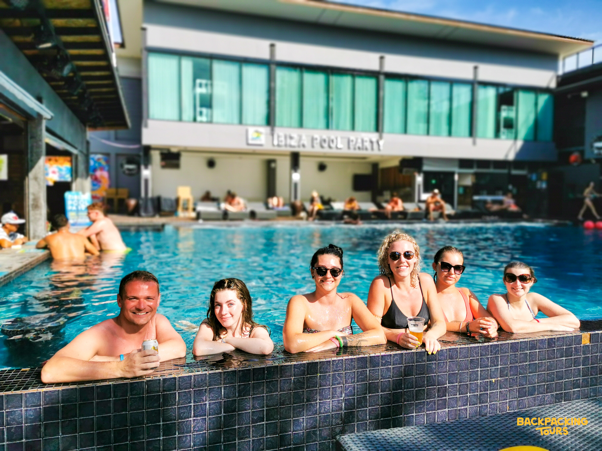 Six happy friends enjoying drinks and sunshine at a lively pool party in Koh Phi Phi, Thailand.