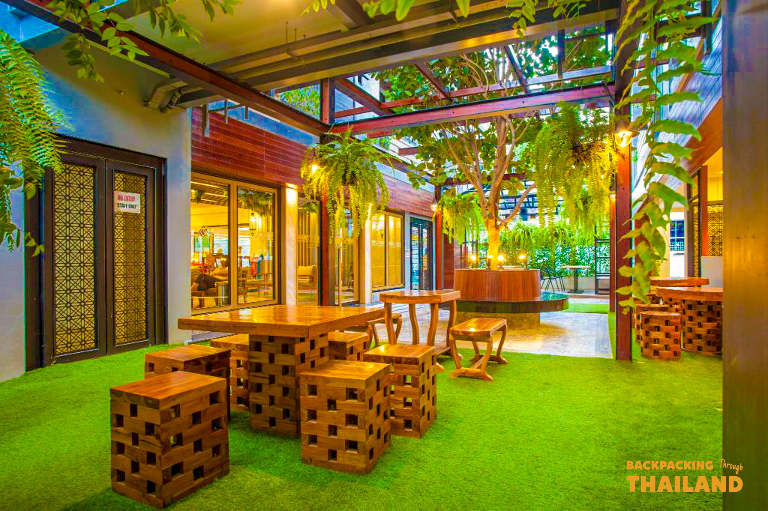 A vibrant outdoor patio with wooden tables, lush green plants, and warm evening lights in Bangkok.
