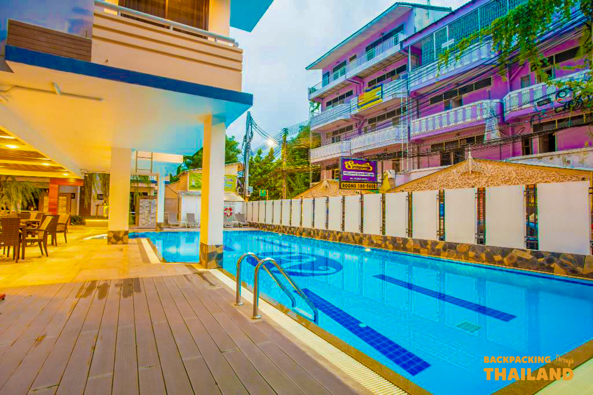 Relax by the inviting hotel swimming pool with a wooden deck and vibrant buildings in Bangkok.