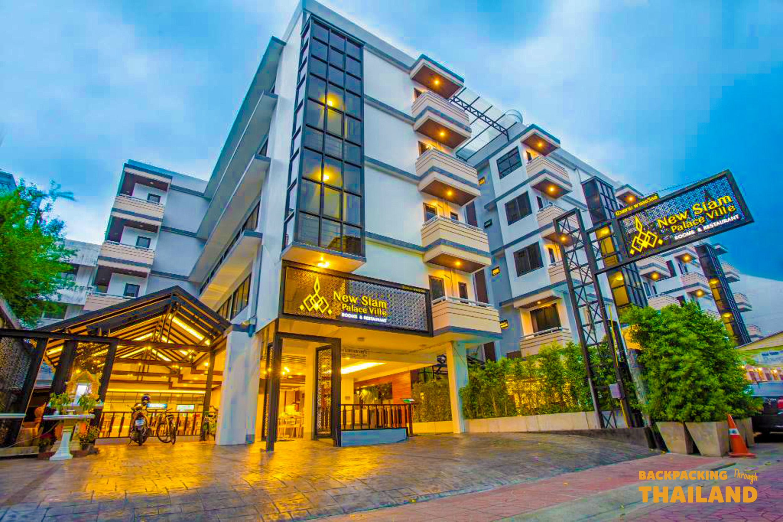 The modern New Siam Palace Ville hotel building with a brightly lit entrance, welcoming guests in Bangkok.