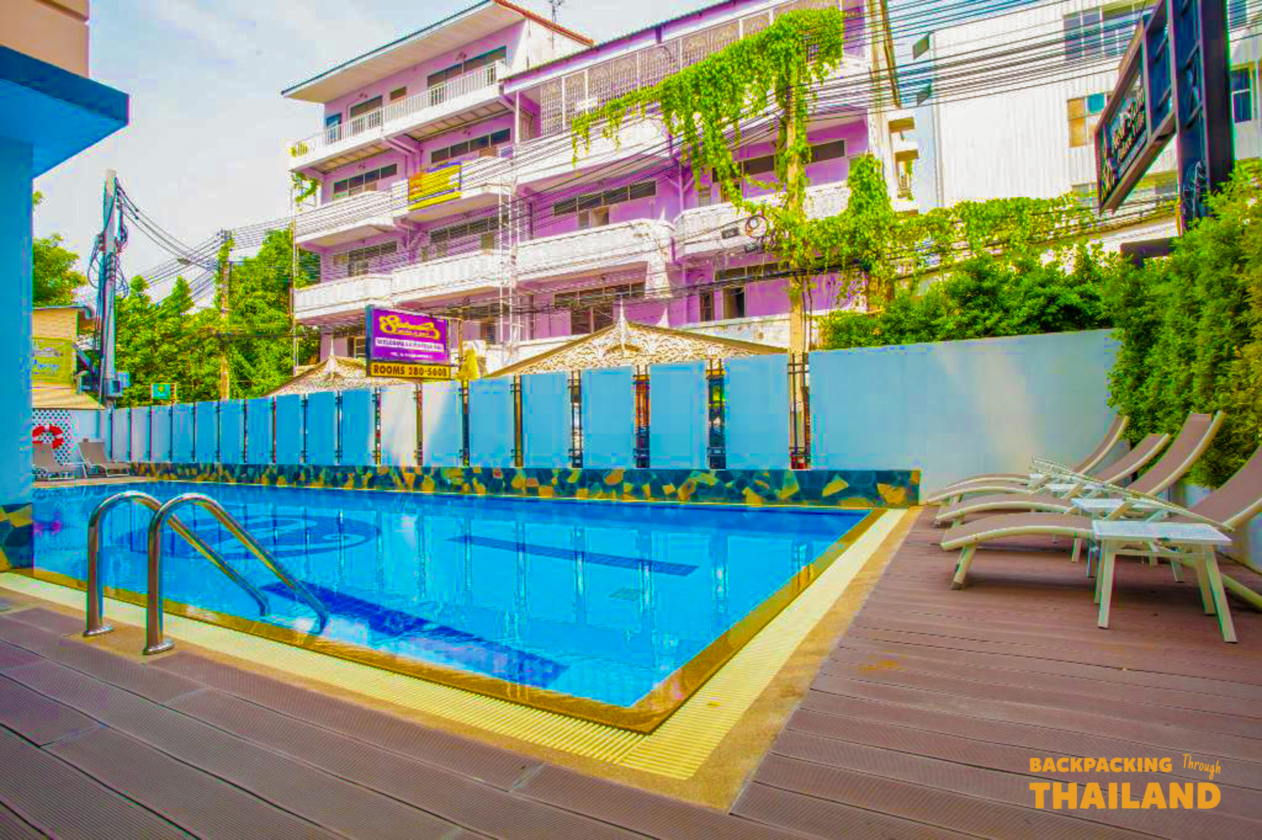 Relaxing hotel swimming pool in Bangkok with sun loungers and a purple building in the background.
