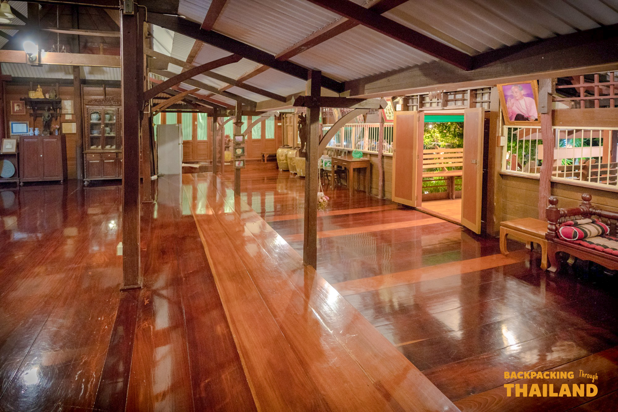 A spacious traditional wooden homestay interior with polished floors and open doors in Amphawa.