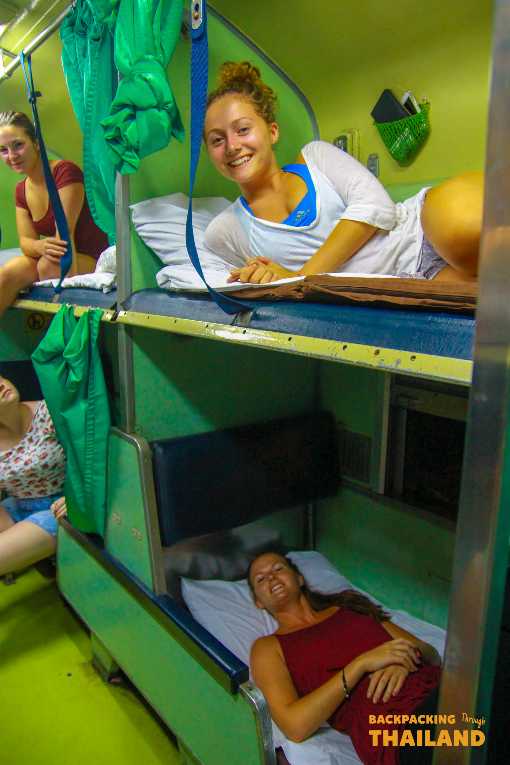 Smiling backpacker girl sitting on bunk bed in Thai night train.