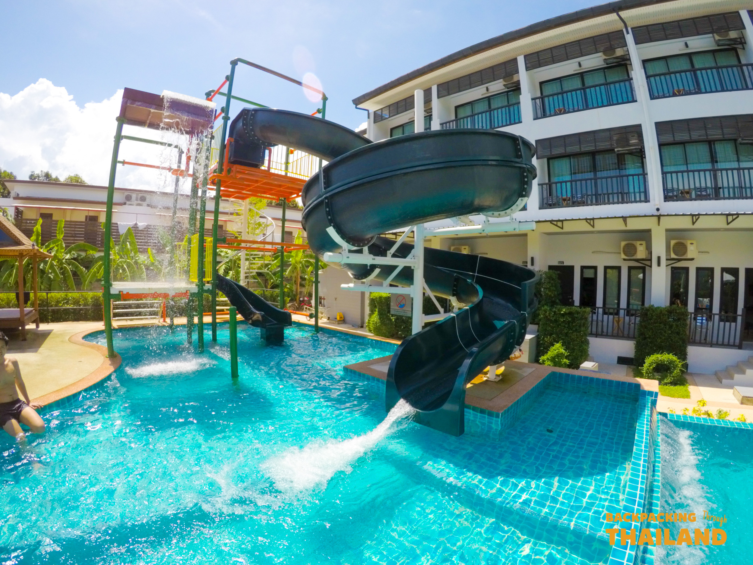 Bright blue swimming pool with exciting water slides at a sunny resort in Krabi, Thailand.
