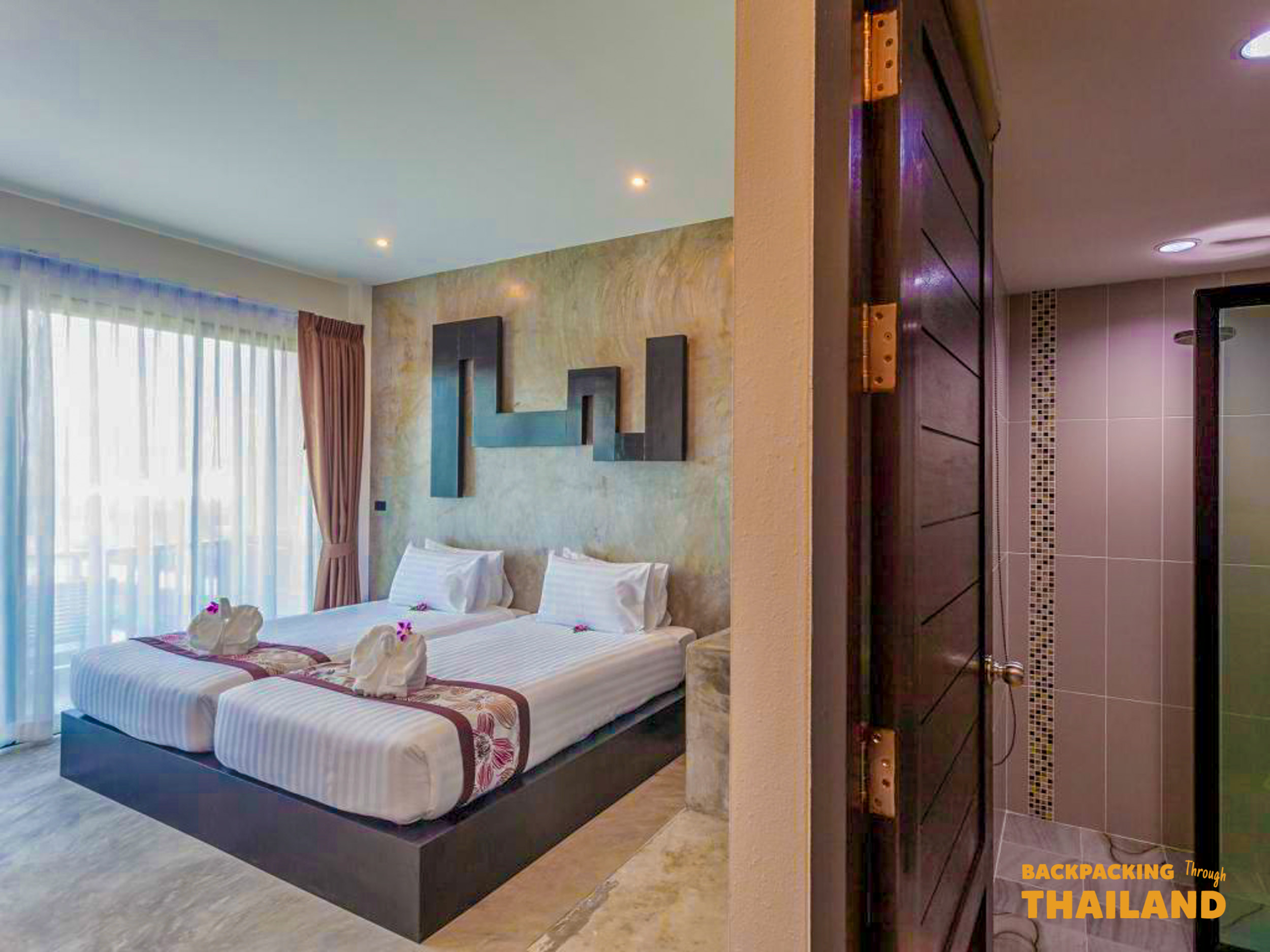 A comfortable twin hotel room with modern decor, swan towel art, and a bright balcony view.