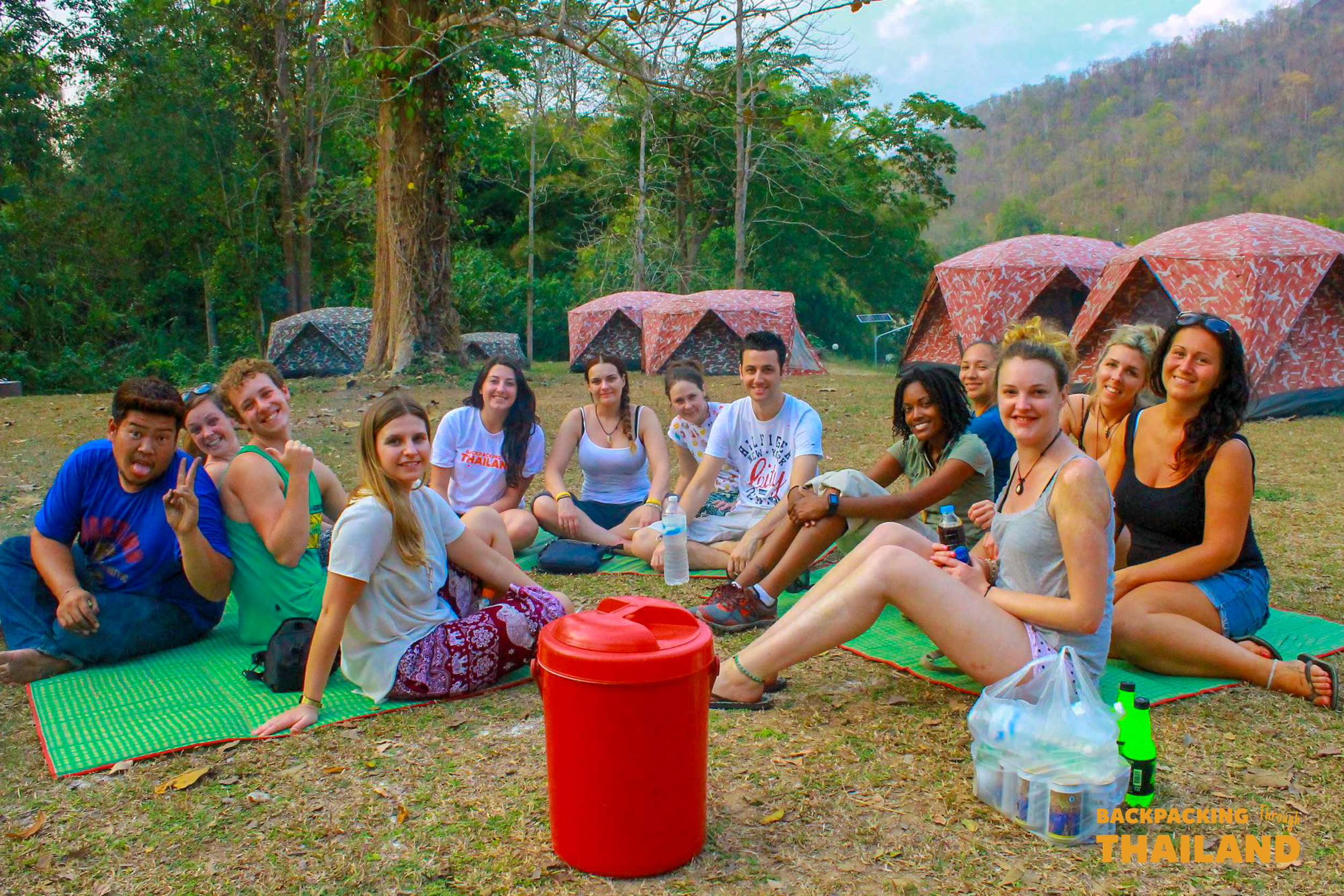 Backpacking group sitting on camping chairs outside their tents enjoying drinks and snacks